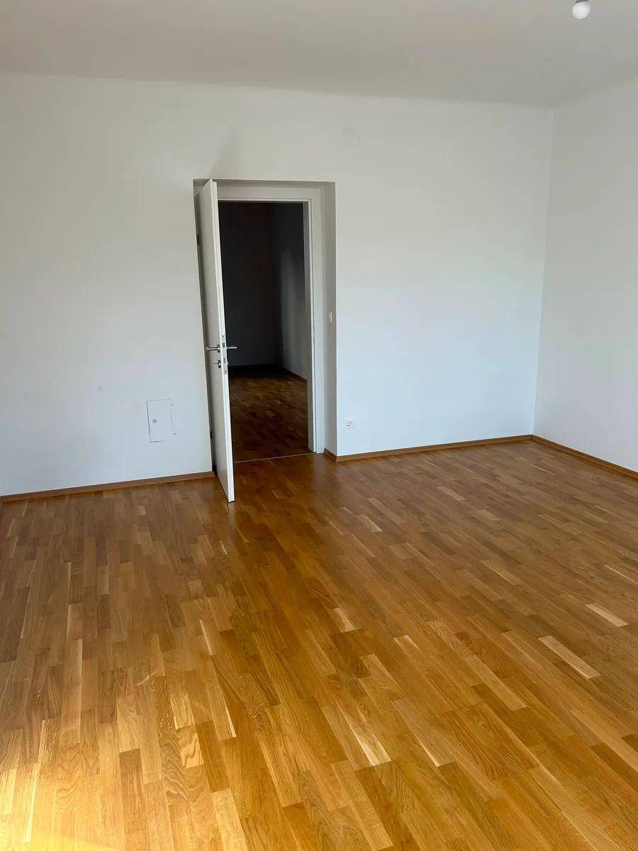 Geräumiges Zimmer mit Parkettboden und einer Tür, die zu einem weiteren Bereich führt.