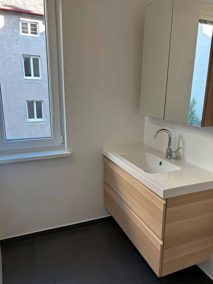 Modernes Badezimmer mit Waschtischunterschrank, Spiegel und Fenster für Tageslicht.
