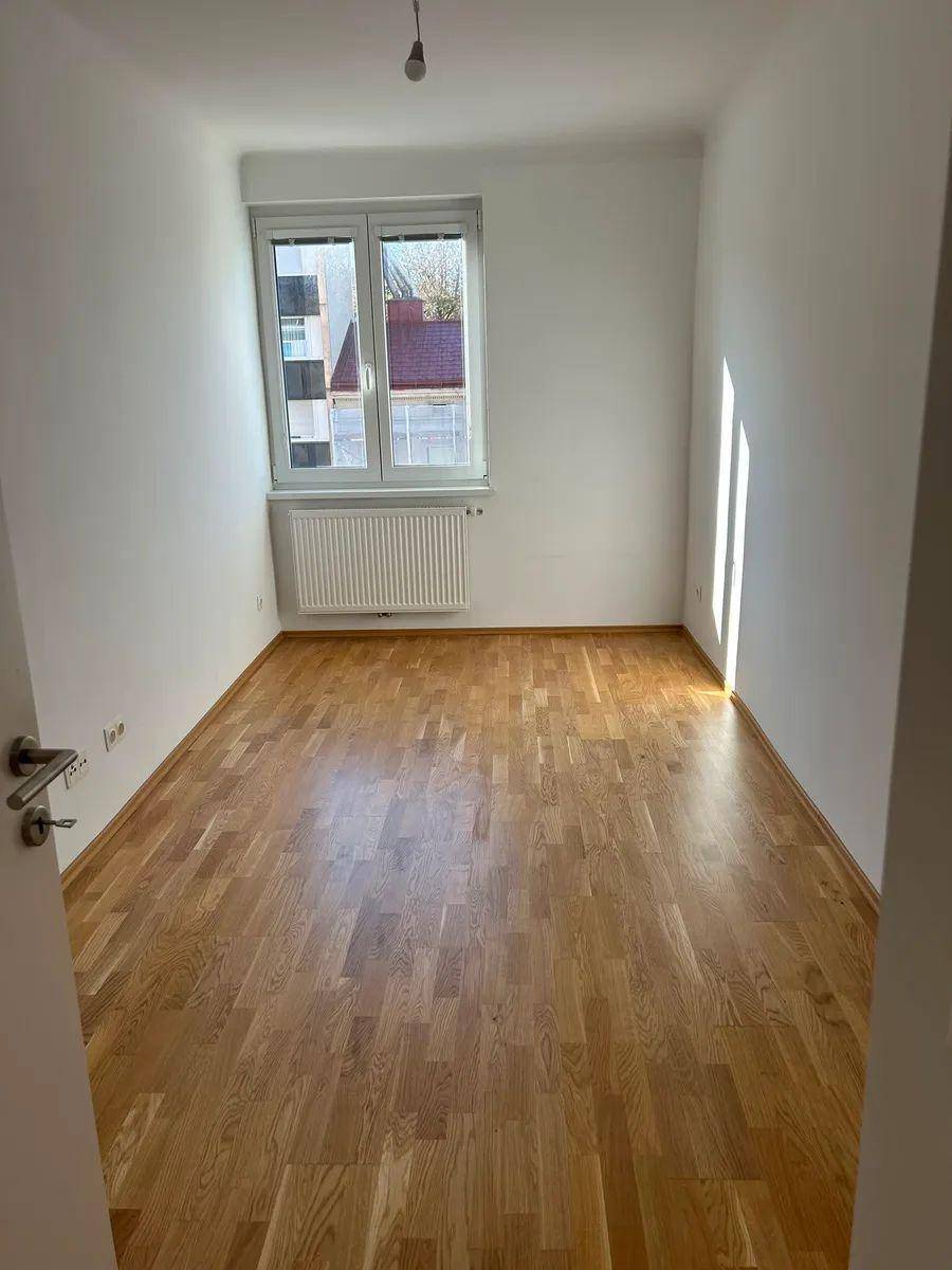 Helles Schlafzimmer mit Parkettboden und einem Fenster, das für eine angenehme Atmosphäre sorgt.