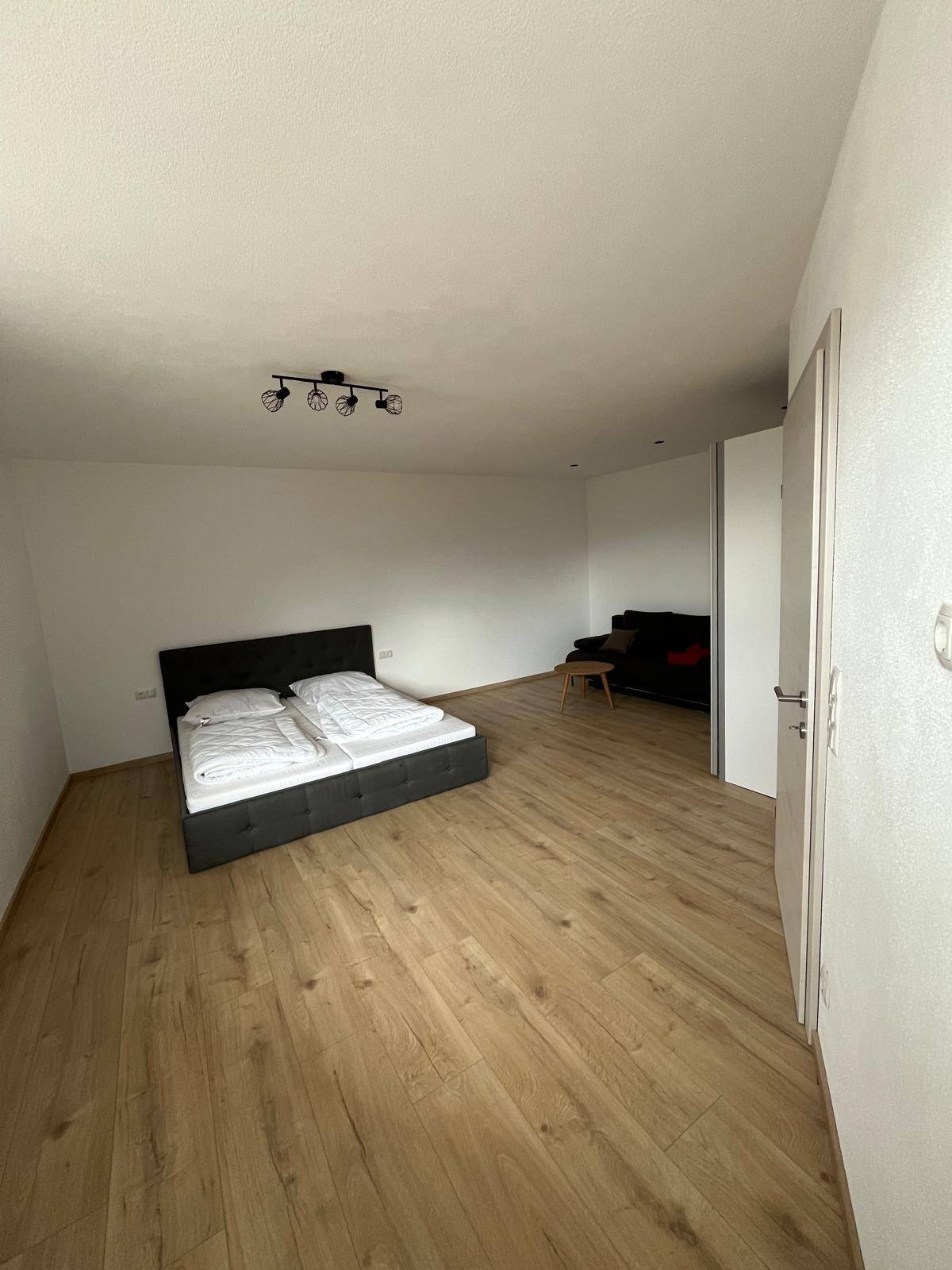 Schlafzimmer mit Doppelbett und Sofa, ausgestattet mit hellem Laminatboden und moderner Beleuchtung.