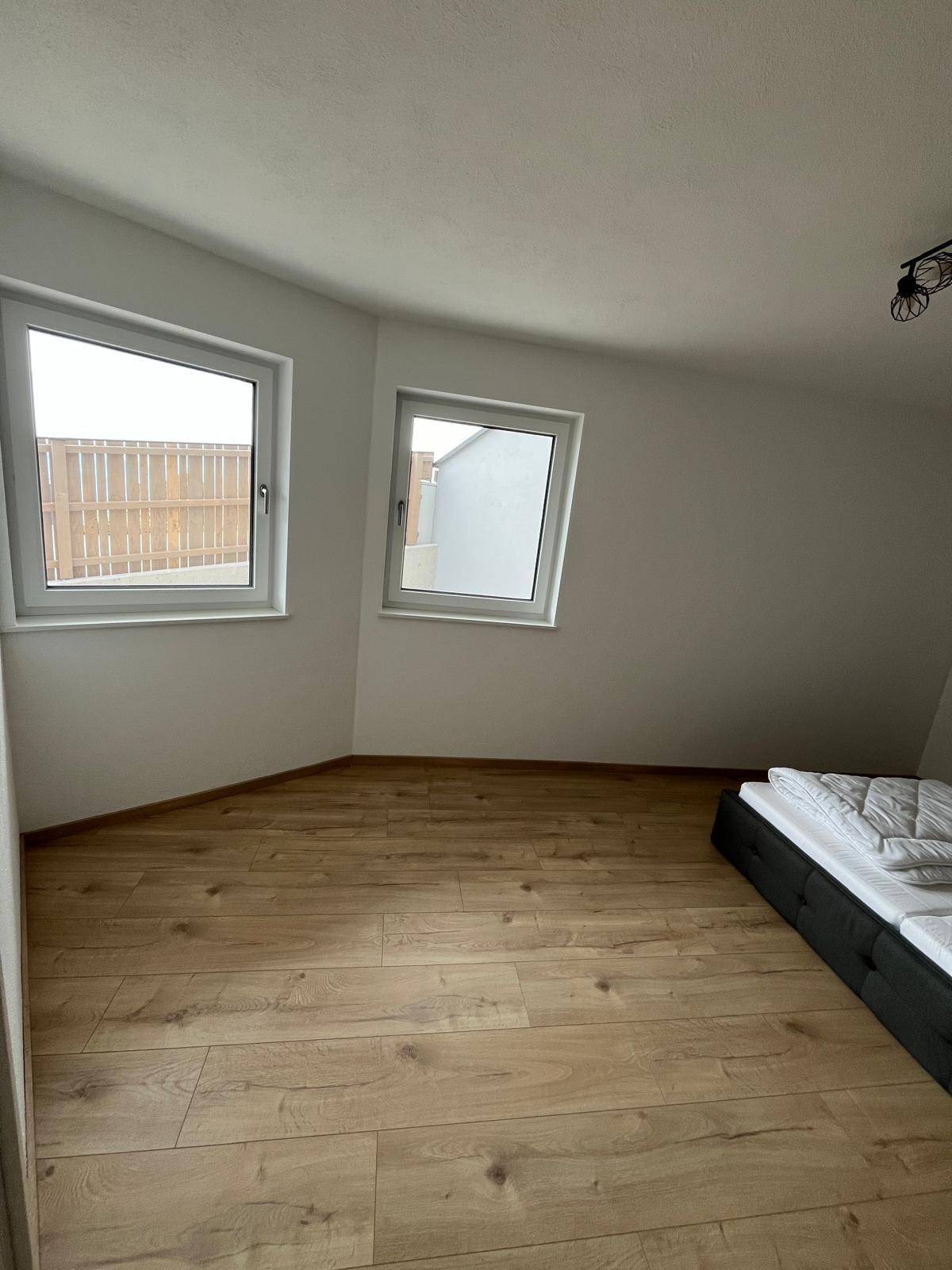 Helles Schlafzimmer mit Doppelbett und zwei Fenstern, die viel Tageslicht hereinlassen.