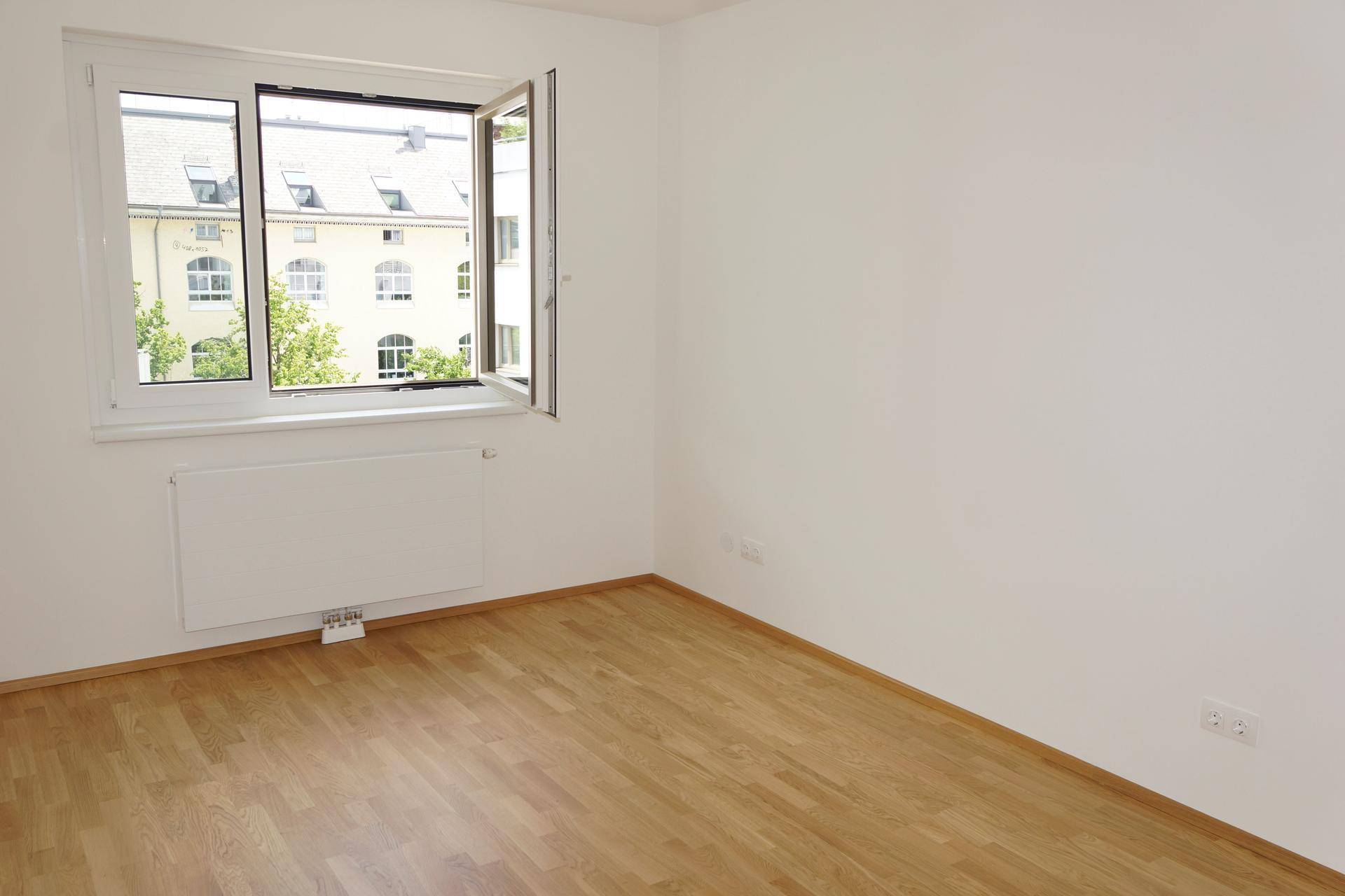 Helles, unmöbliertes Zimmer mit Holzboden und Fenster, das einen Blick auf die Umgebung bietet.