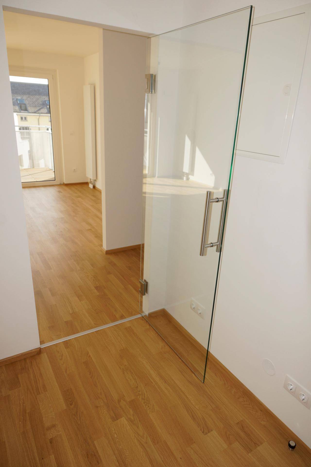 Heller Flur mit Holzboden und einer modernen Glastür, die zu einem weiteren Raum führt.