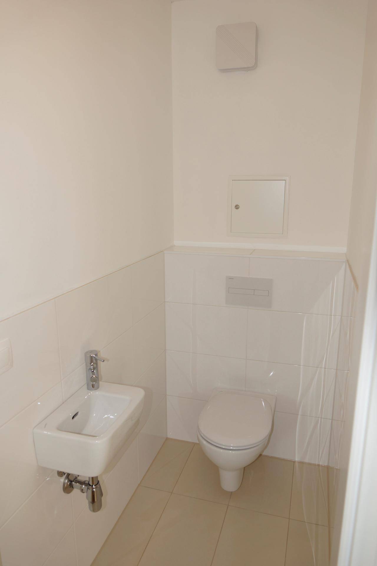 Kleines, hell gefliestes Gäste-WC mit wandhängender Toilette und kompaktem Waschbecken.