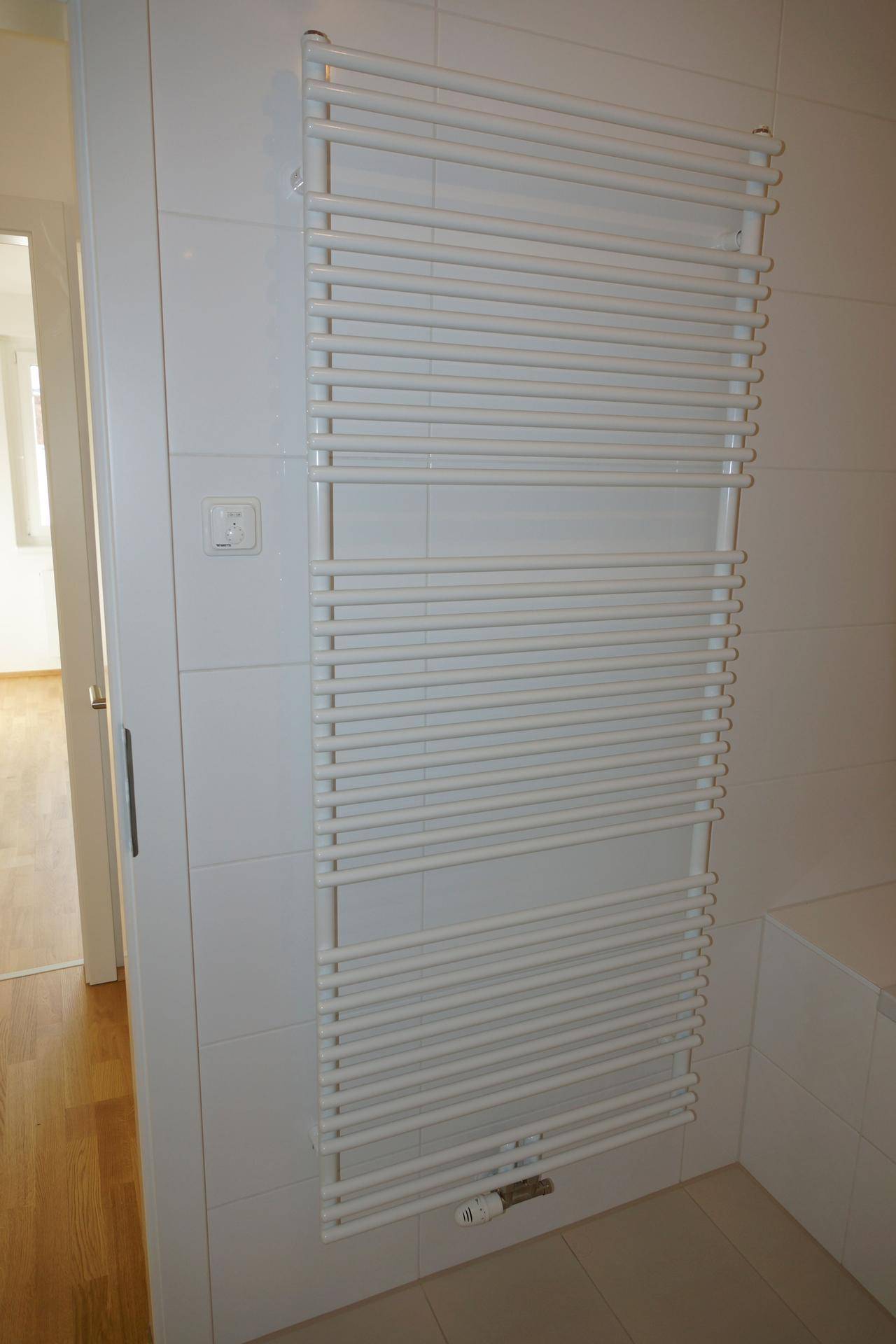 Weißer Handtuchheizkörper an einer gefliesten Wand im Badezimmer, sorgt für warme Handtücher.