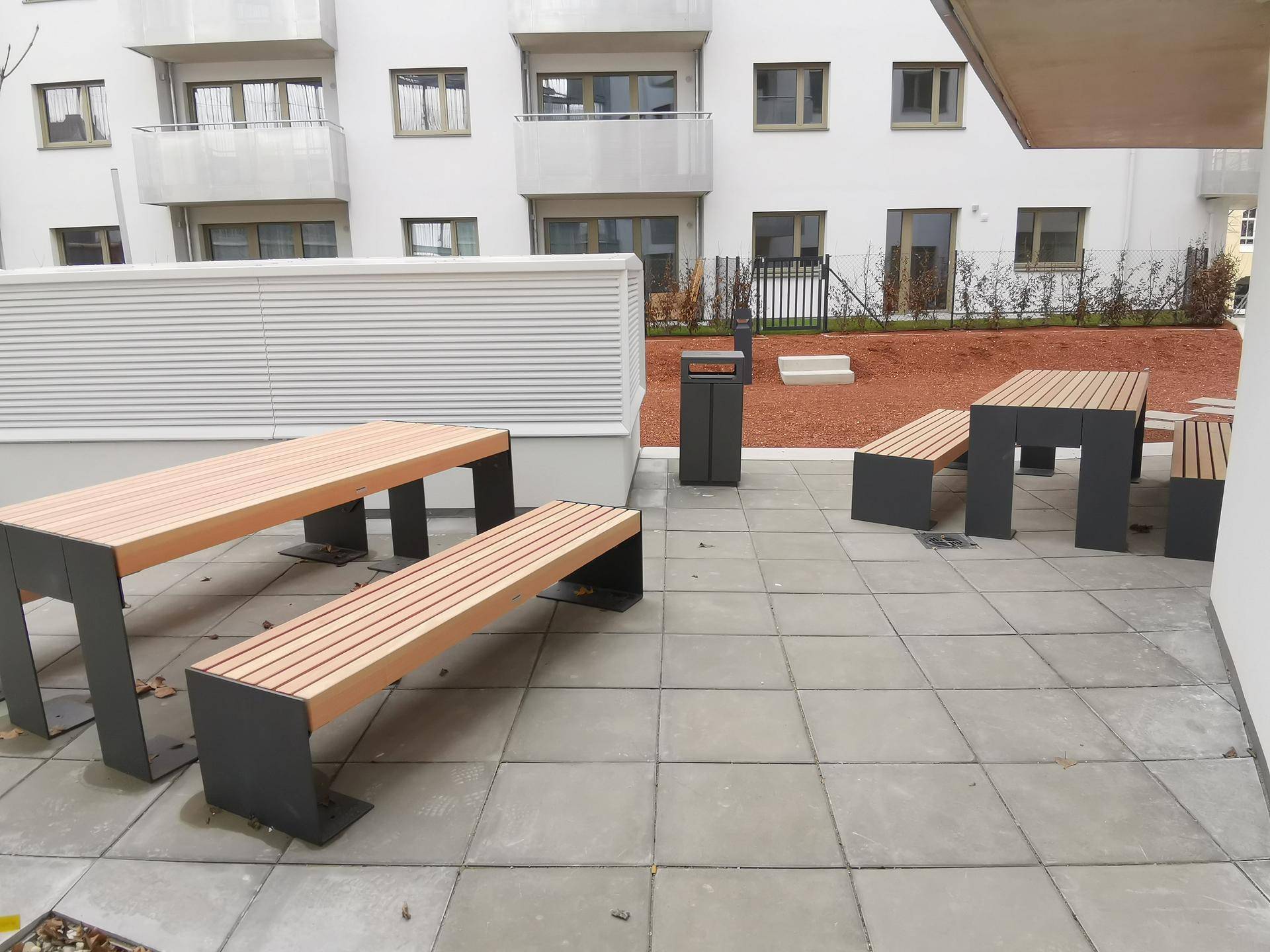 Gepflasterter Außenbereich mit Holzbänken und Tischen, ideal für gemeinschaftliche Nutzung.