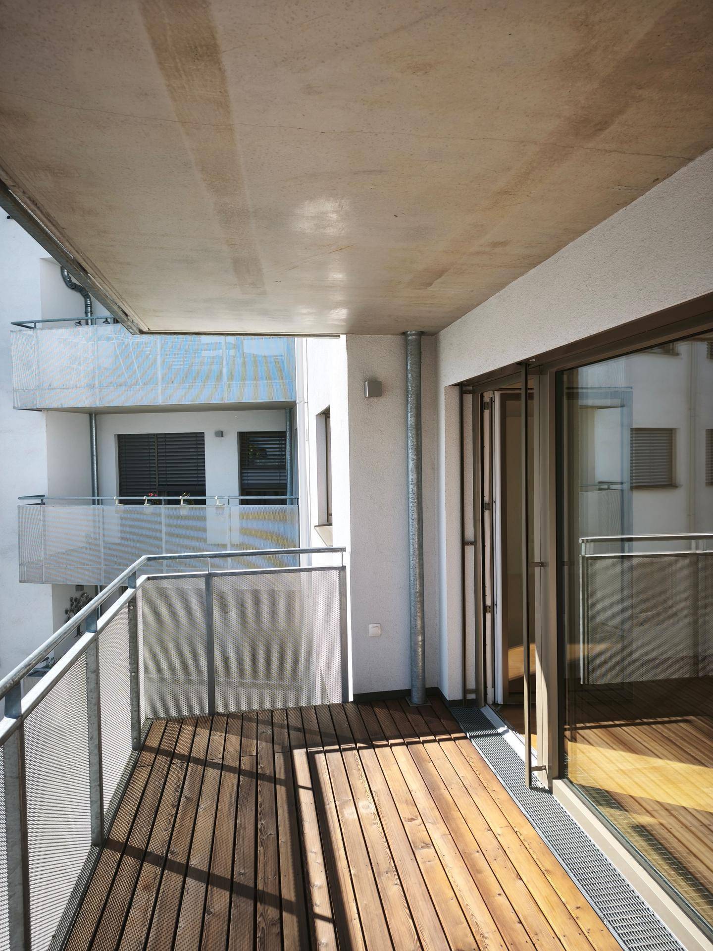 Geräumiger Balkon mit Holzdielen und moderner Metallbrüstung, umgeben von der Architektur des Gebäudes.