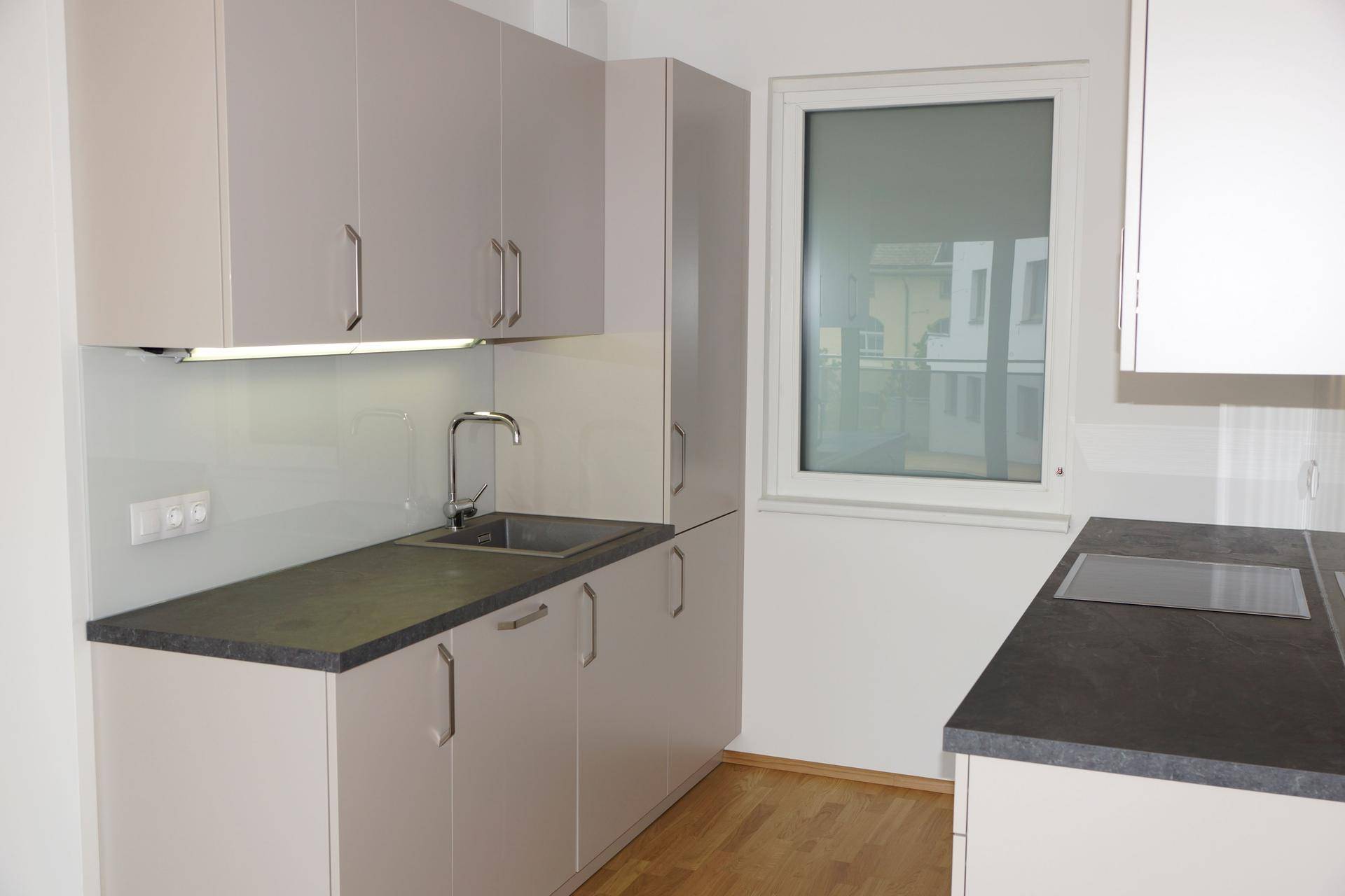 Moderne Küche mit hellgrauen Schränken, dunkler Arbeitsplatte und Induktionskochfeld neben einem Fenster.