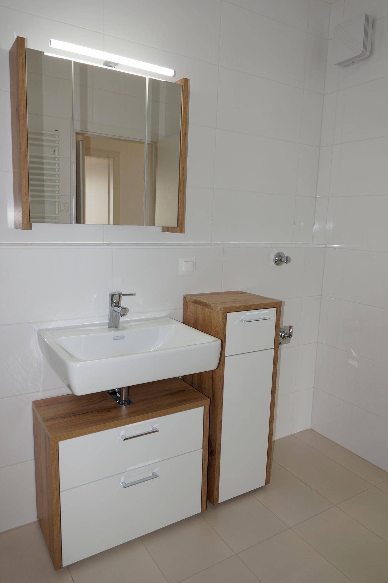 Modernes Badezimmer mit Waschtisch, Holzunterschränken und Spiegelschrank, alles in hellen Tönen gehalten.
