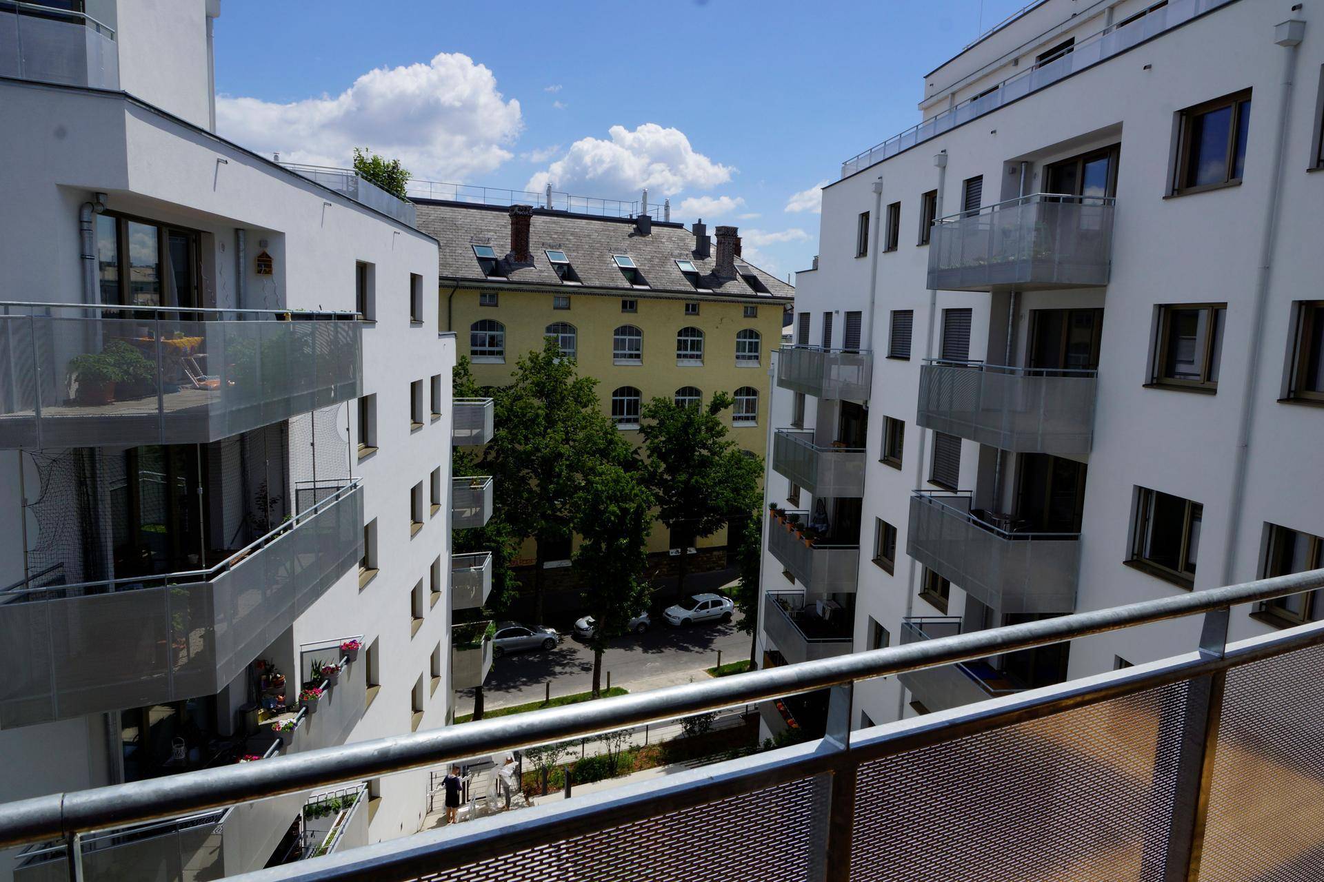Blick von einem Balkon auf einen Innenhof mit Bäumen und die Fassaden moderner sowie älterer Gebäude.