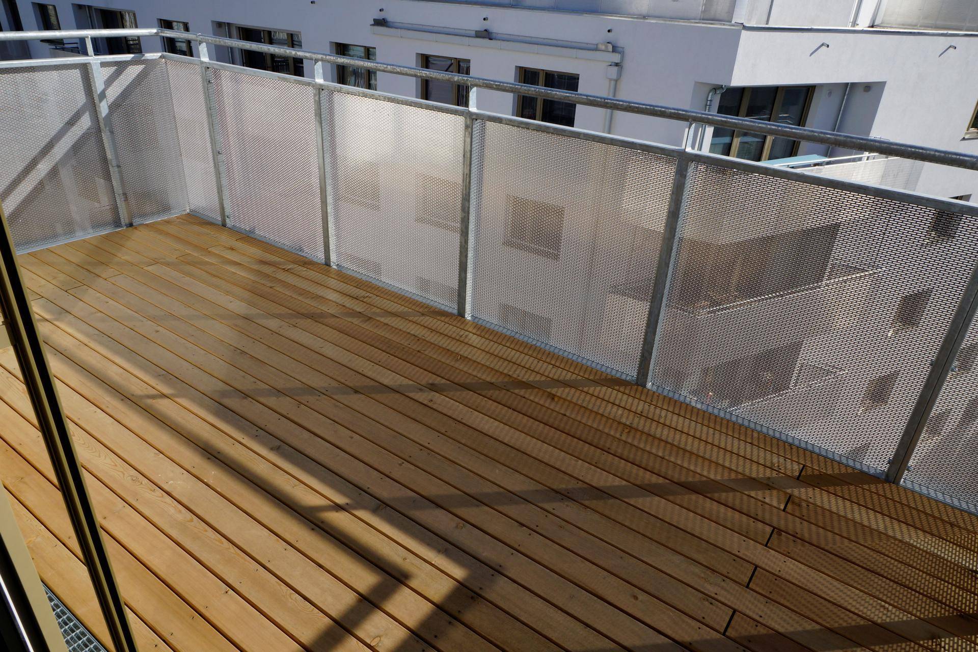 Balkon mit Holzdielenboden und moderner Metallbrüstung, bietet Blick auf umliegende Gebäude.
