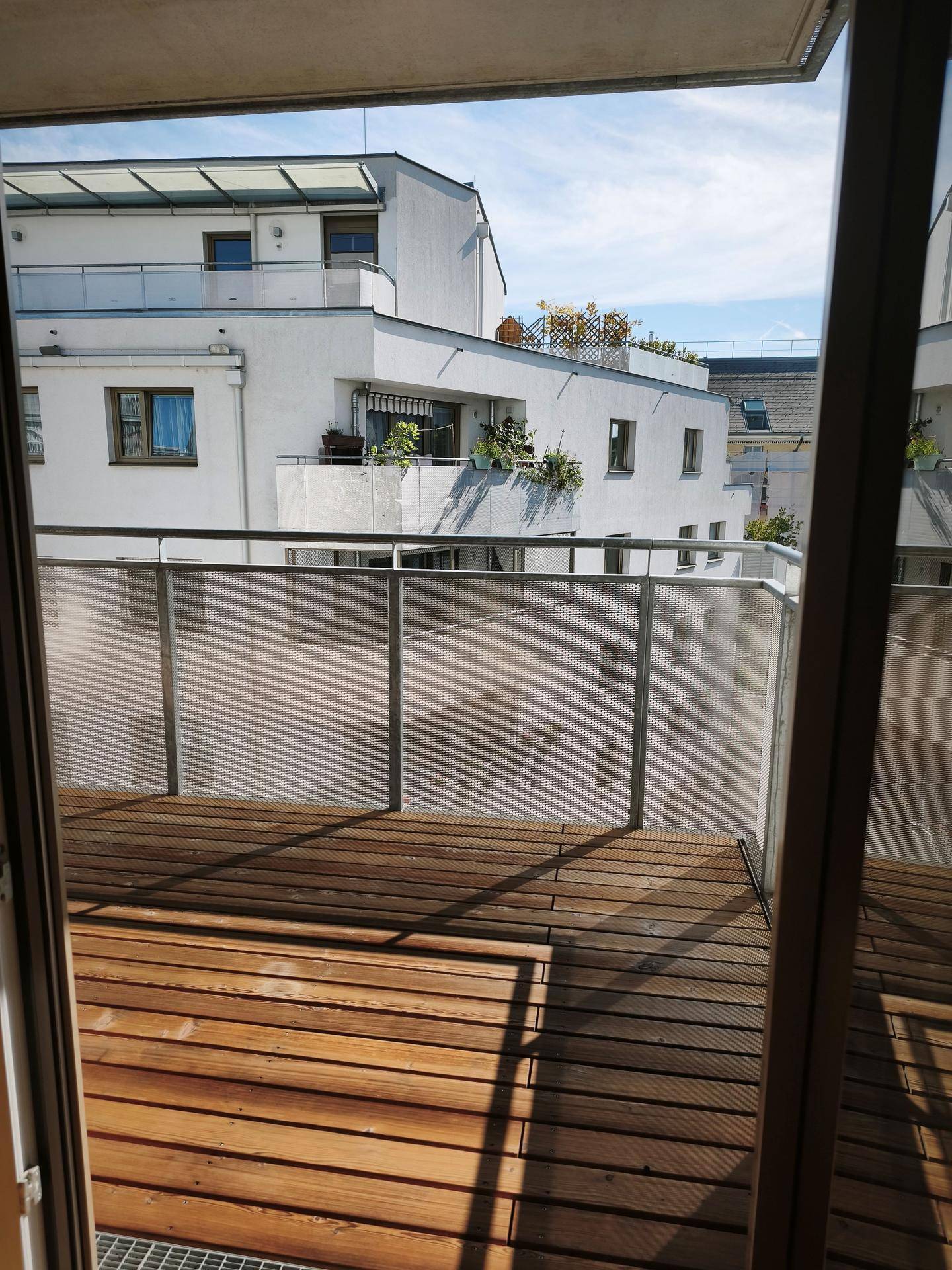 Blick von einem Balkon mit Holzdielen auf die modernen weißen Fassaden der umliegenden Gebäude.