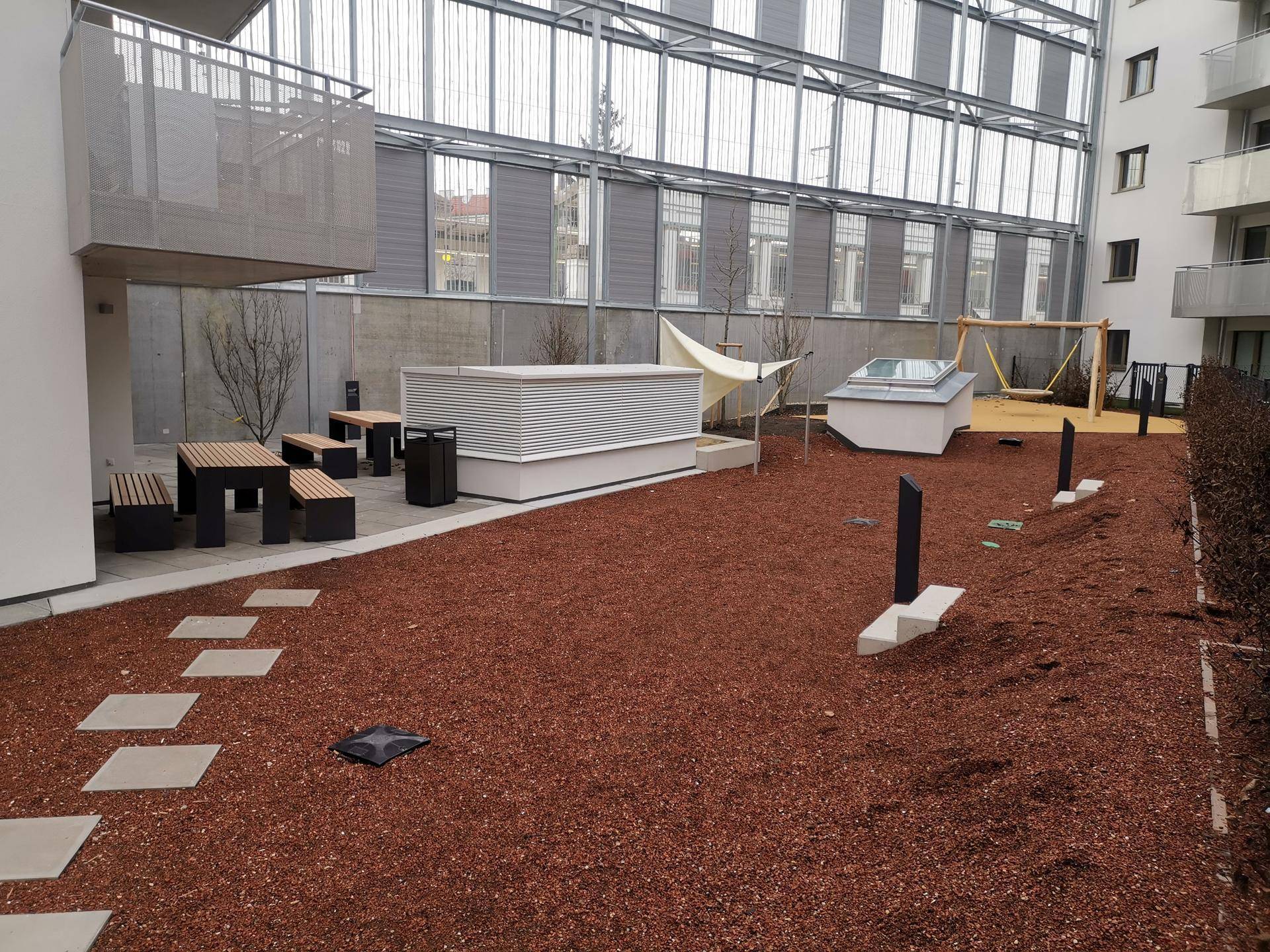 Gemeinschaftlicher Außenbereich mit rotem Mulch, Sitzgelegenheiten und einem kleinen Spielplatz.