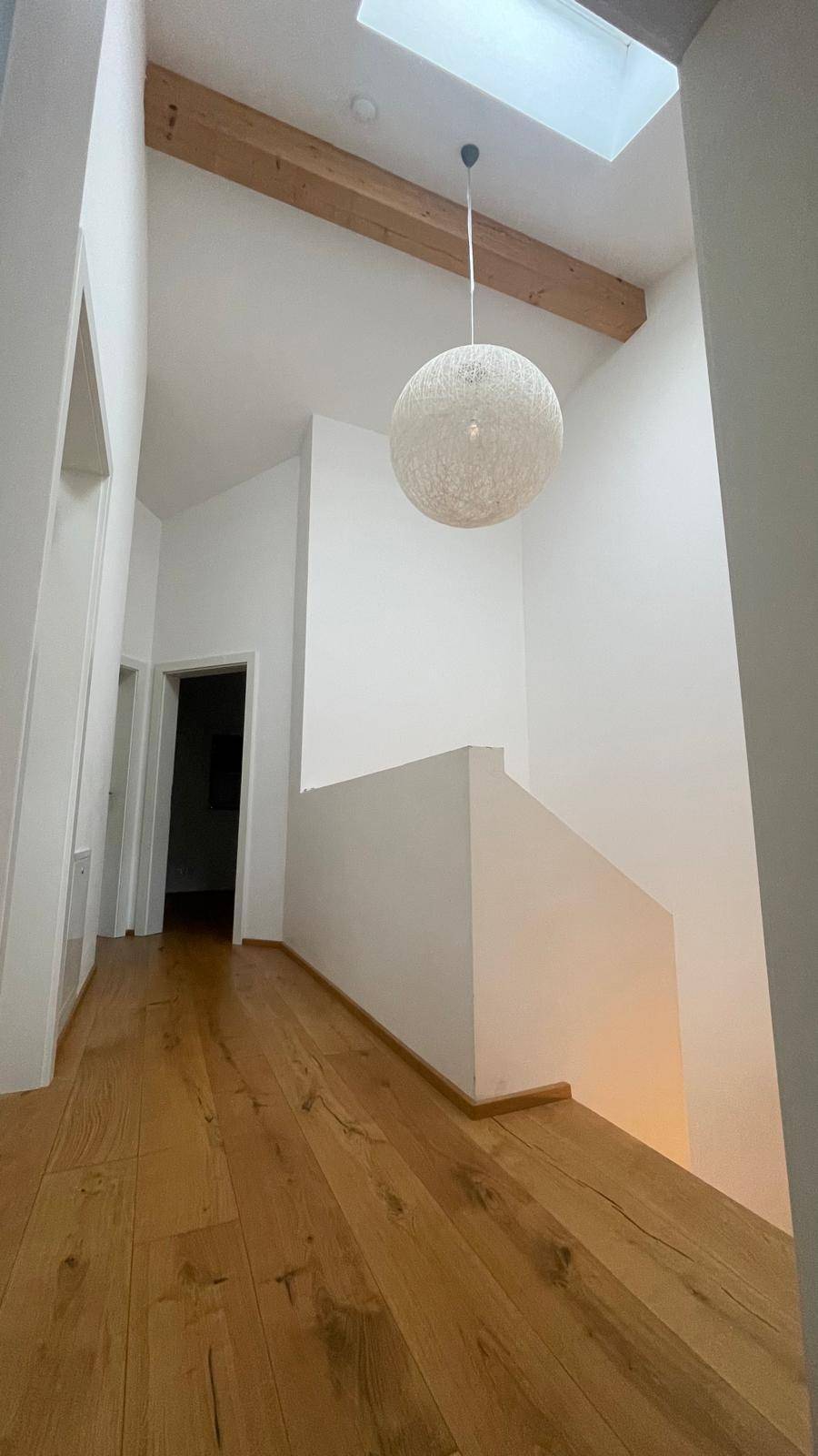 Heller Flur mit Holzboden, sichtbarem Holzbalken und Oberlicht für natürliches Licht.