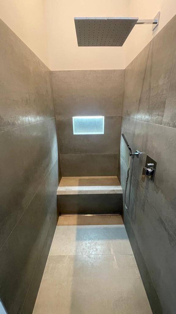 Stilvolle begehbare Dusche mit Regenduschkopf und integrierter Sitzbank.