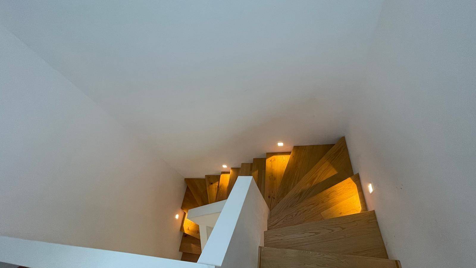Moderne Holztreppe mit integrierter Beleuchtung und weiß gestrichenen Wänden.