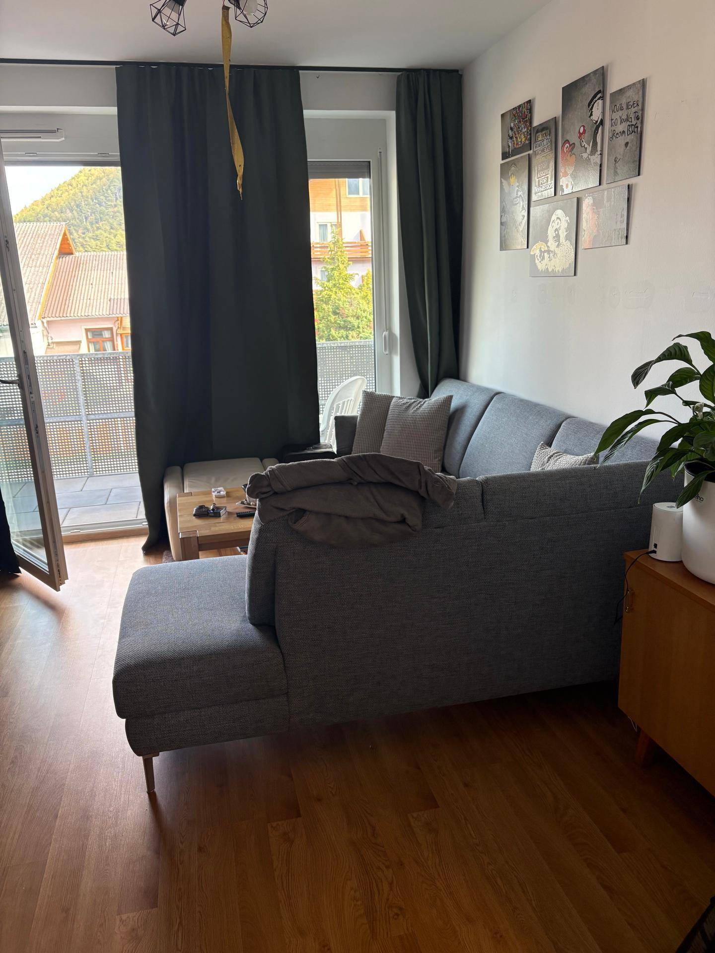 Helles Wohnzimmer mit grauem Ecksofa und Balkonzugang, bietet einen schönen Blick ins Grüne.