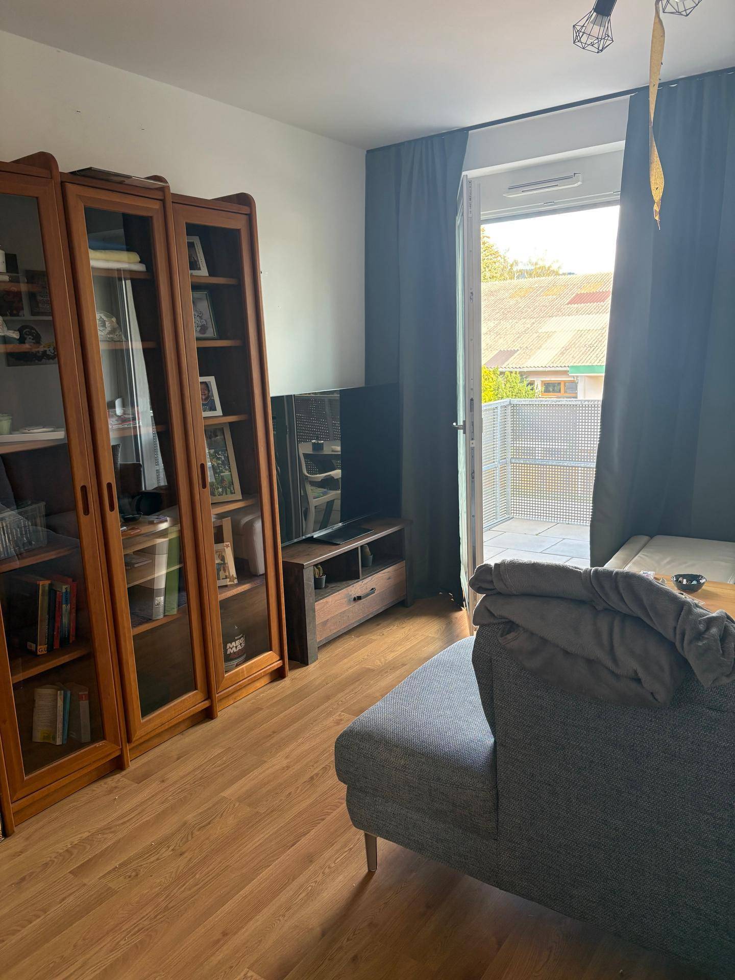 Wohnzimmer mit Holzvitrinen und Fernseher, bietet direkten Zugang zu einem Balkon.