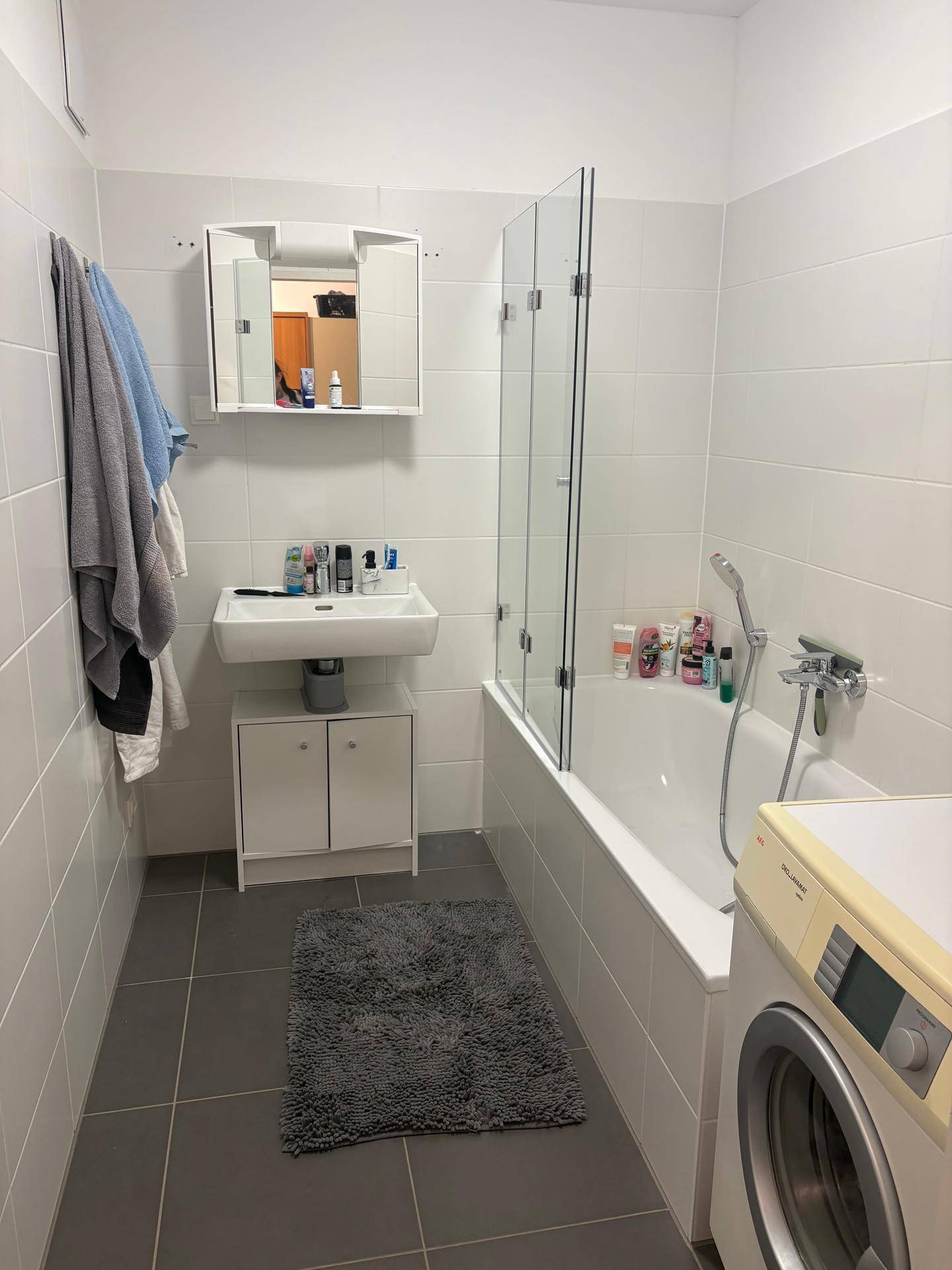 Modernes Badezimmer mit Badewanne, Duschwand, Waschbecken und Spiegelschrank, inklusive Waschmaschine.