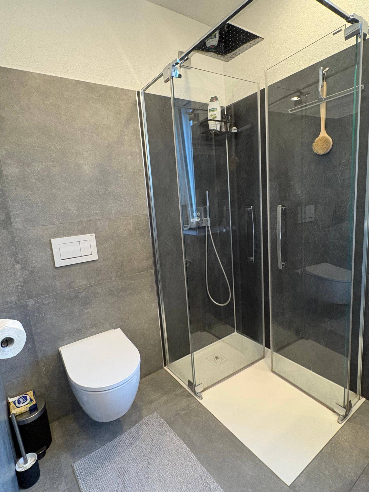 Modernes Badezimmer mit grauen Fliesen, bodengleicher Dusche und wandhängendem WC, minimalistisch und funktional.
