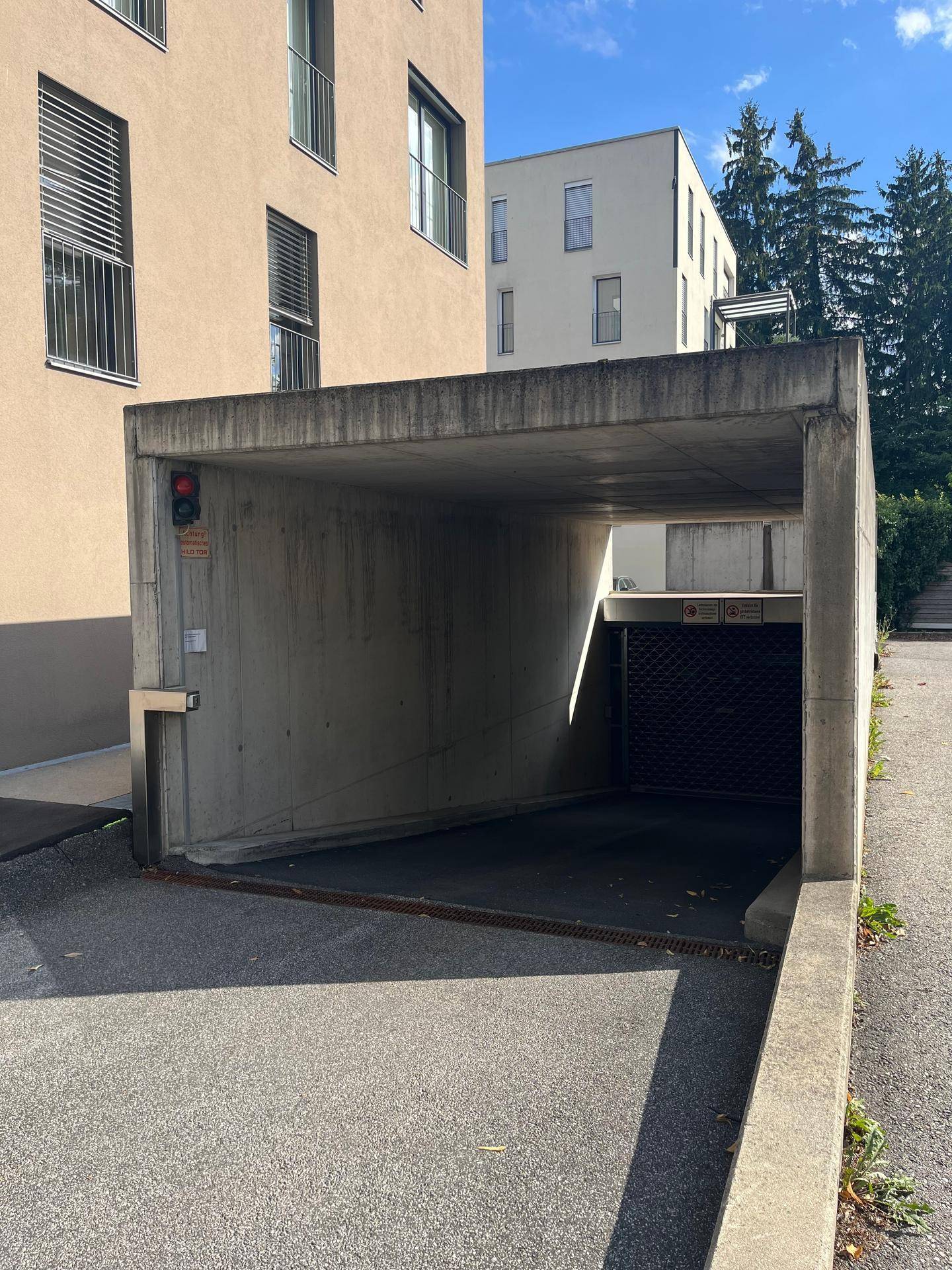 Eingang zu einer Tiefgarage aus Beton neben einem modernen Gebäude unter blauem Himmel.