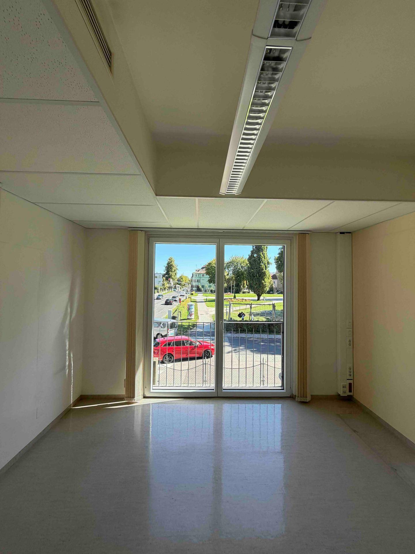 Leerer Raum mit einem großen Fenster, das eine weite Aussicht auf die Straße und die gegenüberliegende Bebauung bietet.