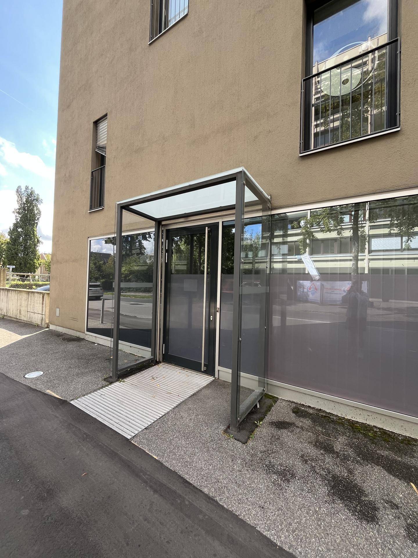 Haupteingang des Gebäudes mit Glasvordach und einer Rampe für barrierefreien Zugang.