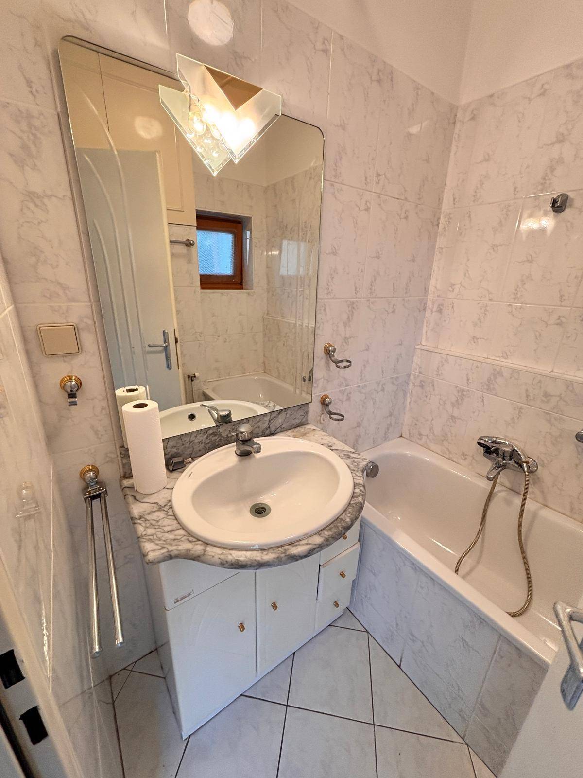Badezimmer im Stil der 80er Jahre mit Badewanne, Einzelwaschbecken und Fenster.