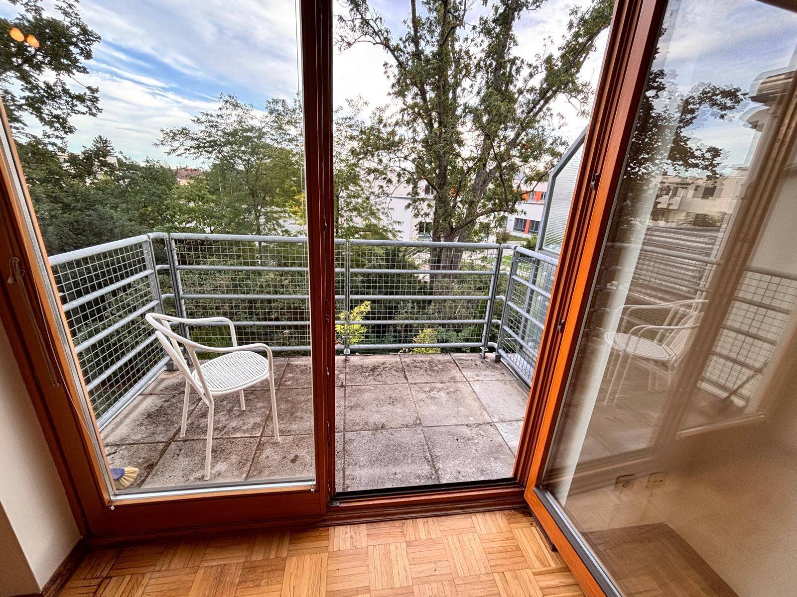 Balkon mit Sitzgelegenheit und weitem Blick auf grüne Bäume und die Umgebung.
