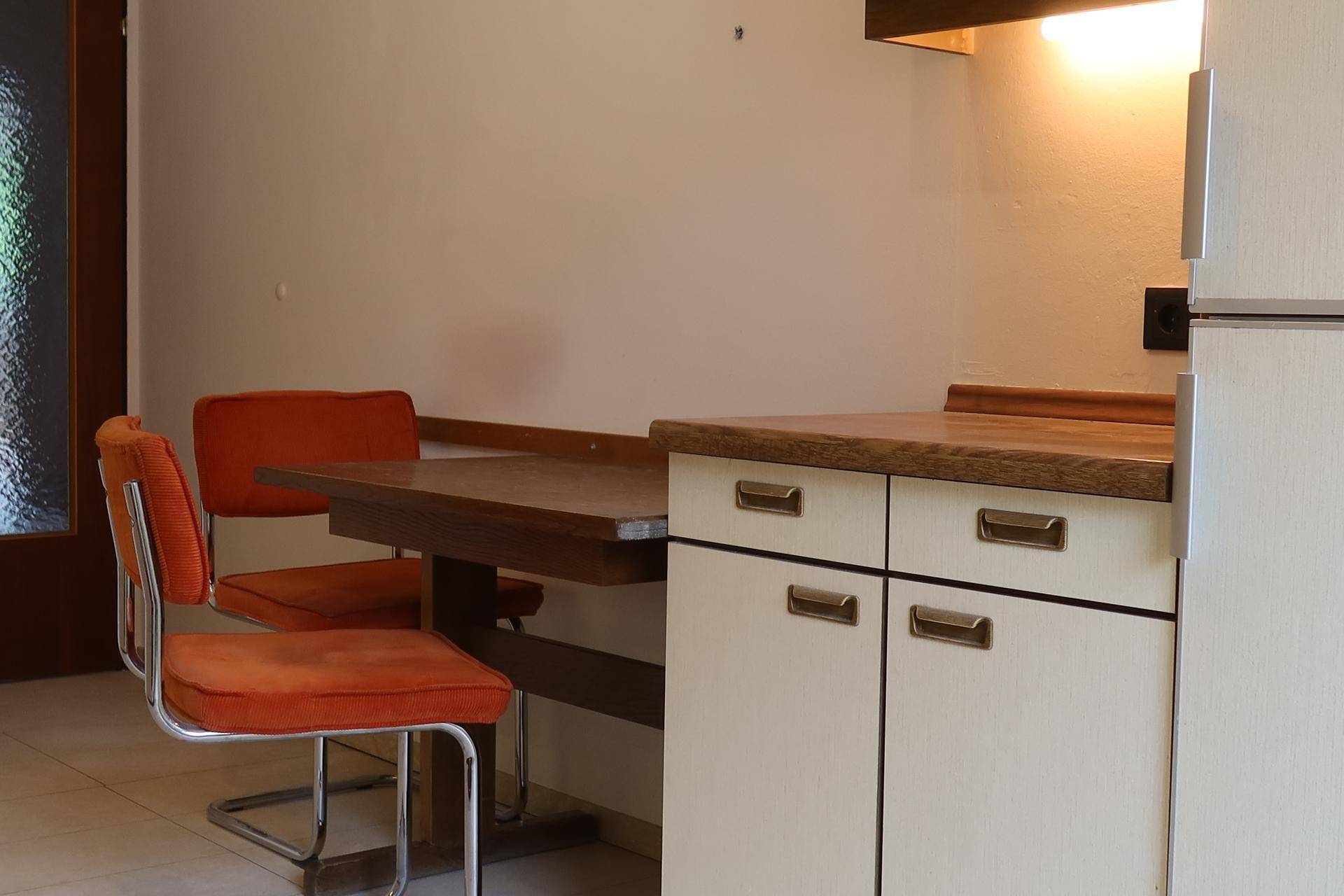 Detailansicht des Essbereichs in der Küche mit Holztisch und orangefarbenen Stühlen.