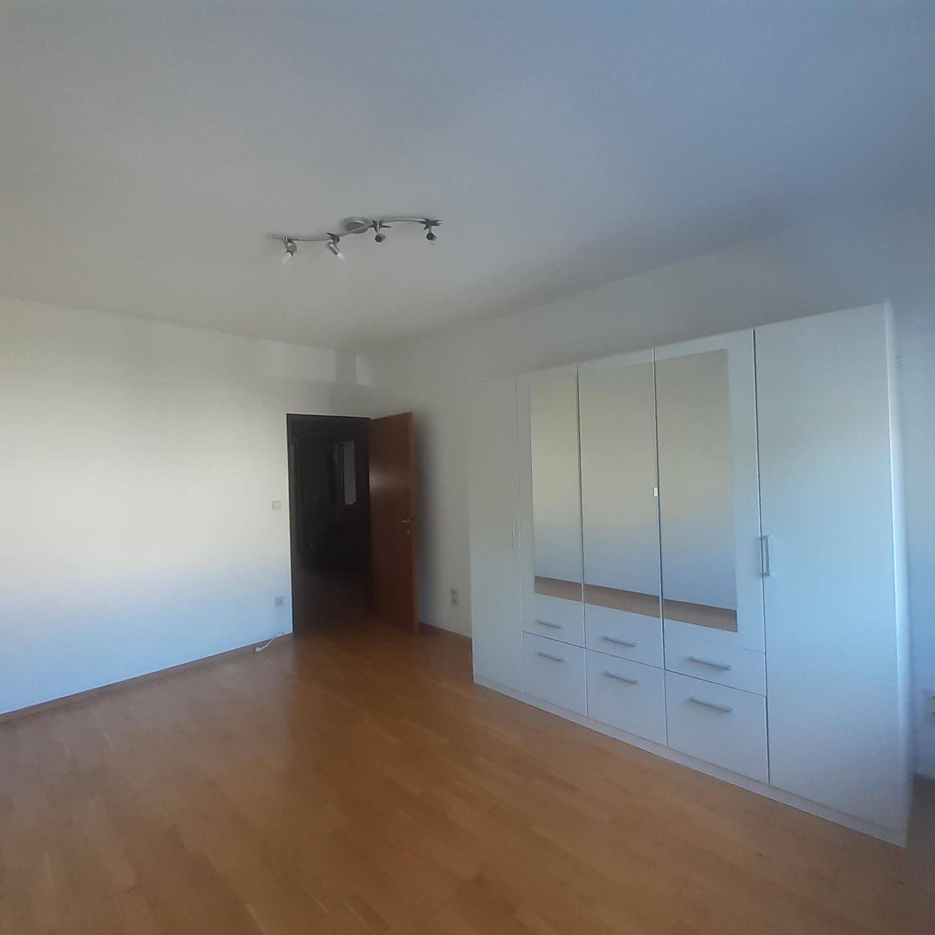 Helles Schlafzimmer mit Parkettboden und einem großen, modernen Spiegelschrank.