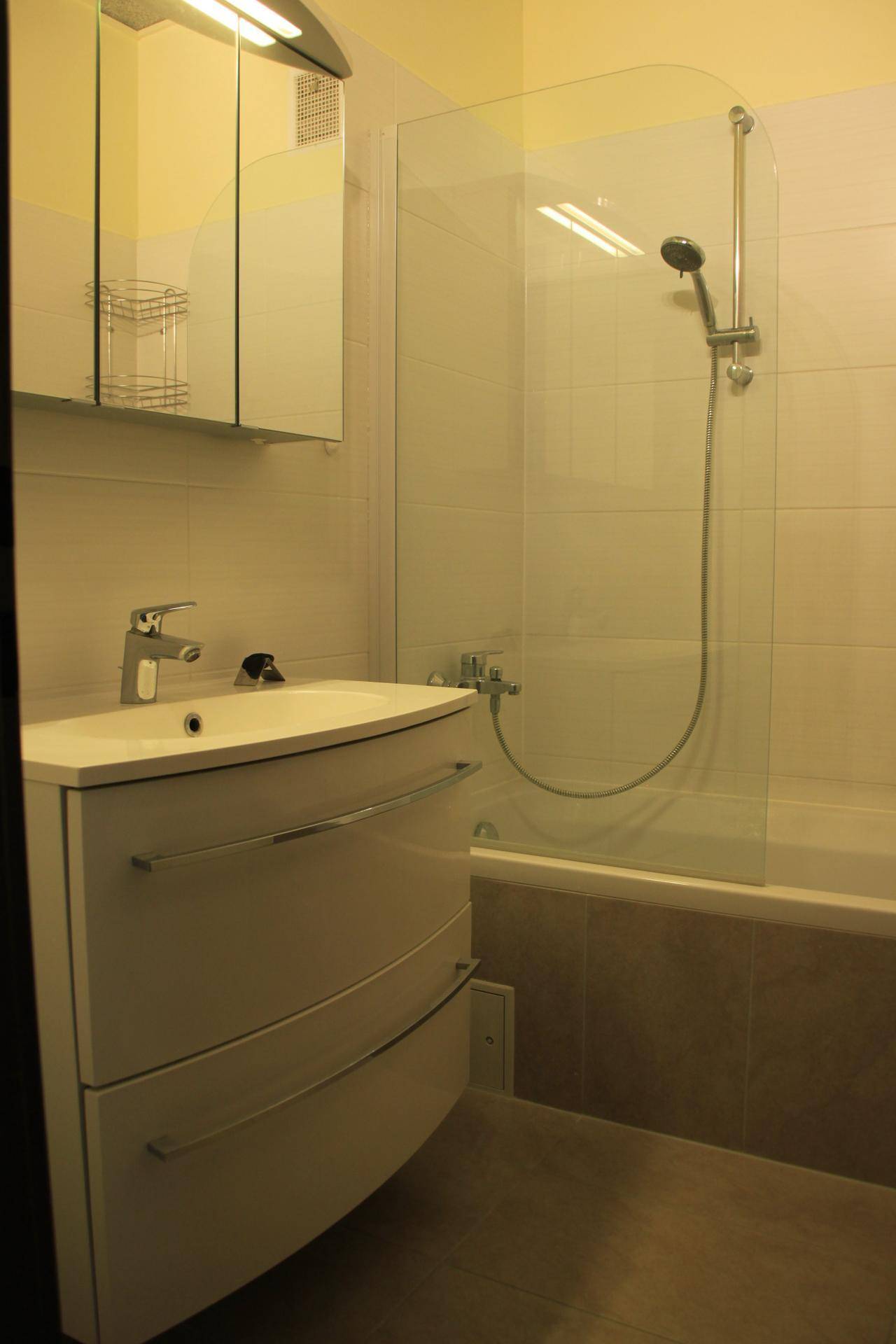 Badezimmer mit Waschtisch, Spiegelschrank und einer Badewanne mit Duschabtrennung.