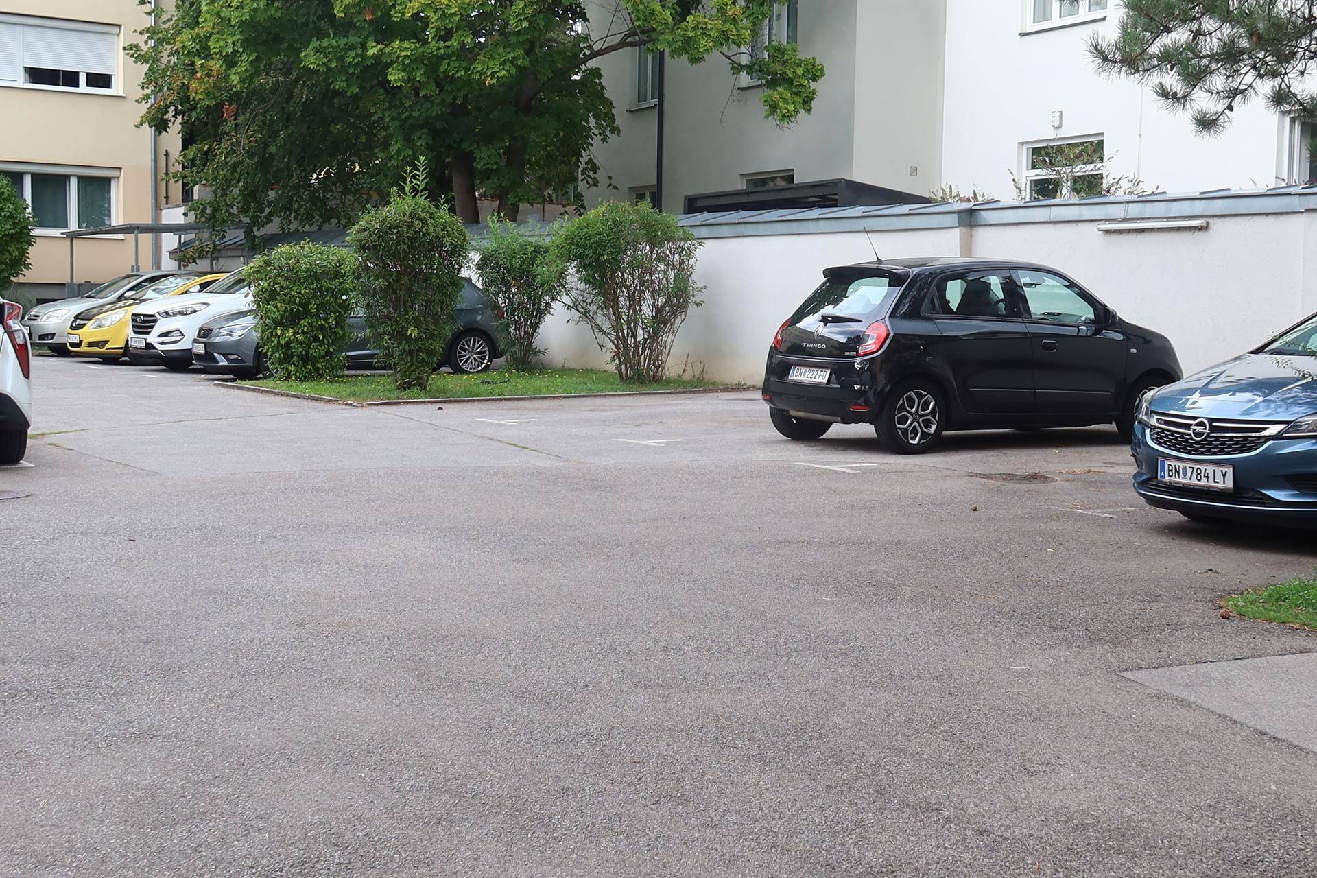 Außenparkplatz mit mehreren Fahrzeugen und Grünflächen in der Wohnanlage.