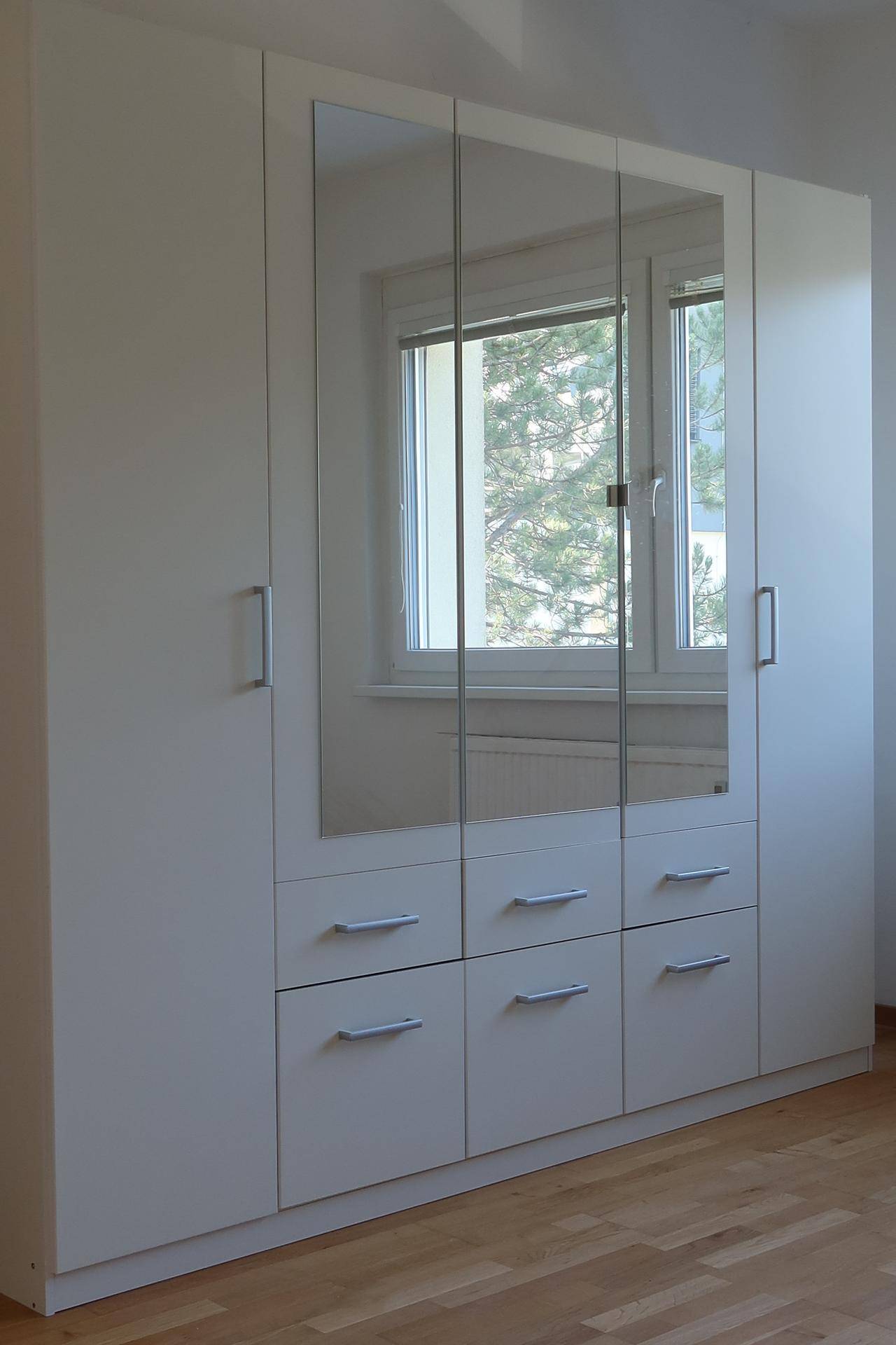 Moderner Spiegelschrank im Schlafzimmer, der das Fenster und die grüne Umgebung reflektiert.