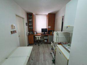 Kleines Untersuchungszimmer mit Schreibtisch, Einbauschränken und einer Untersuchungsliege.