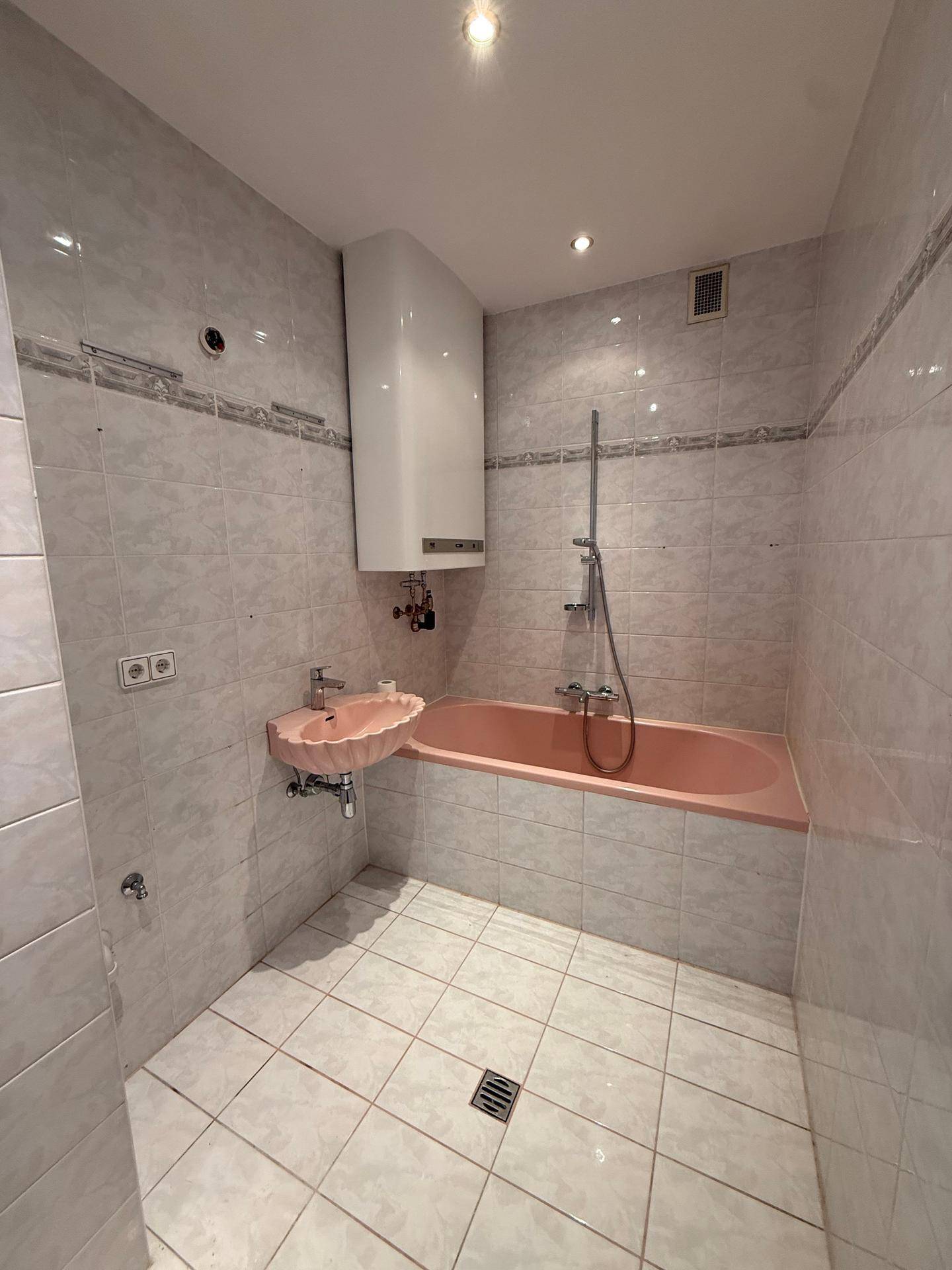 Badezimmer mit rosa Badewanne, Waschbecken und hellen Fliesen an Wänden und Boden.