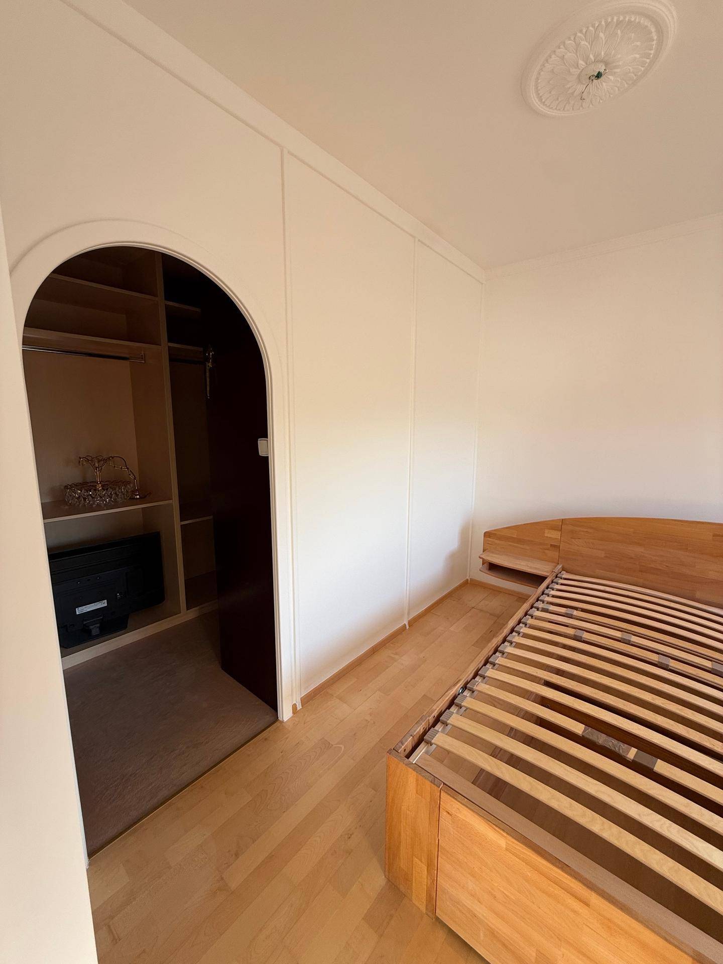 Schlafzimmer mit Holzbettrahmen und praktischen, integrierten Wandschränken für viel Stauraum.
