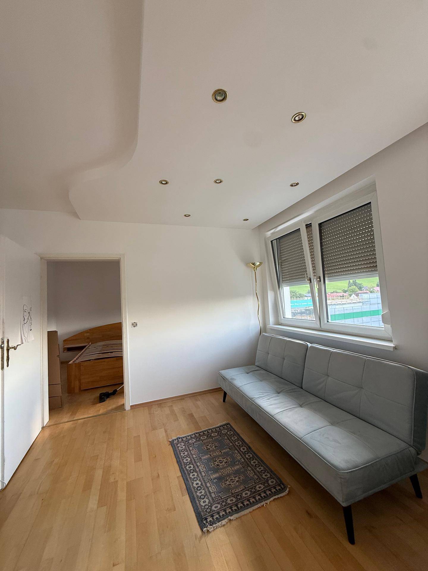 Heller Wohnbereich mit Holzfußboden, modernem Sofa und Zugang zu einem weiteren Zimmer.