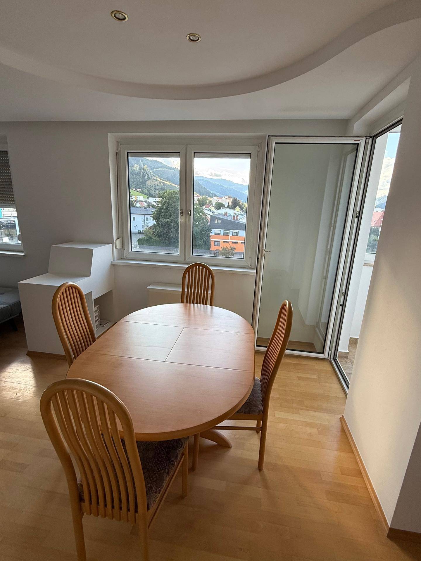 Gemütlicher Essbereich mit Holztisch, Stühlen und Zugang zu einem Balkon mit Bergblick.