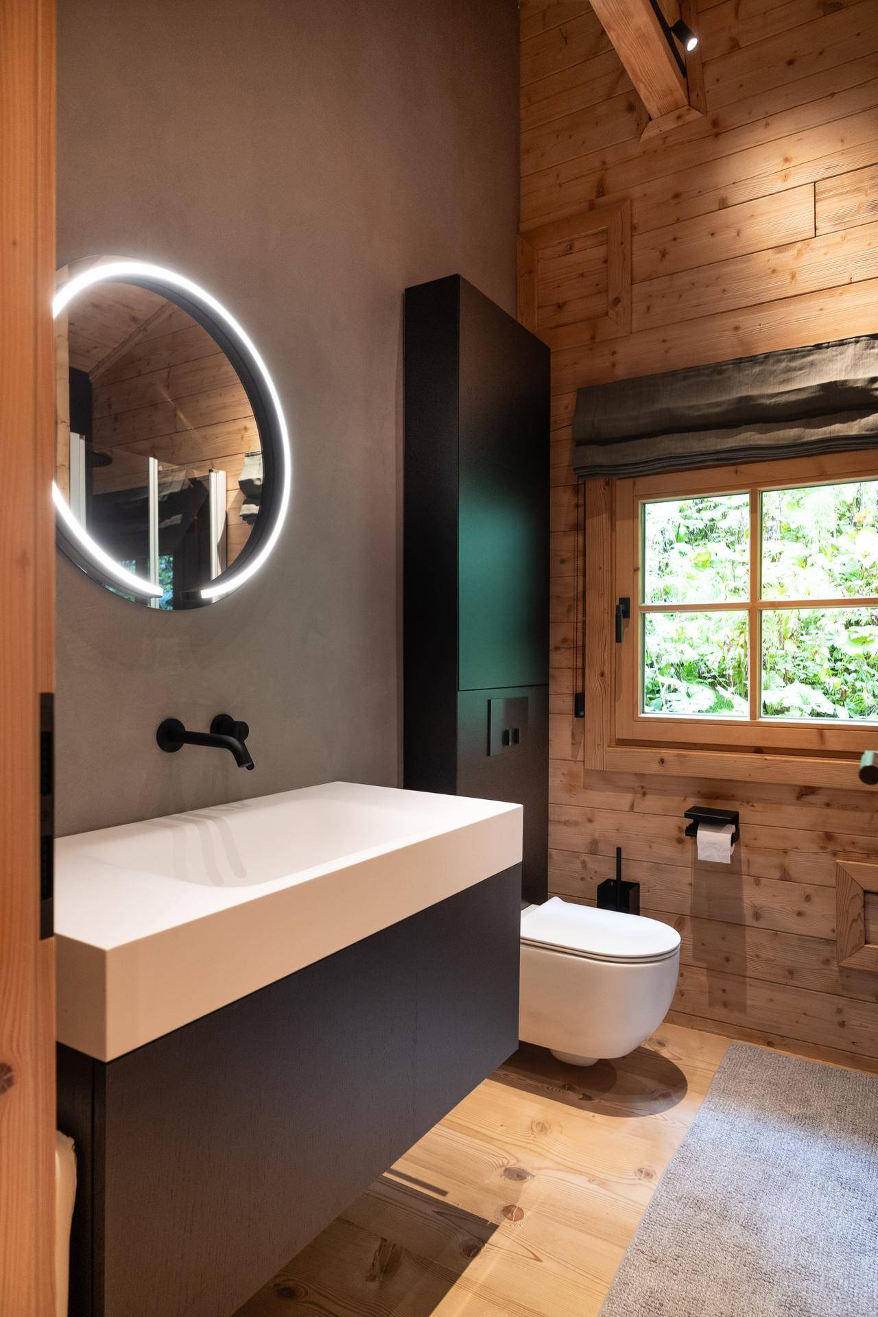 Modernes Badezimmer mit Holzvertäfelung, runder Spiegelleuchte und wandhängendem WC.