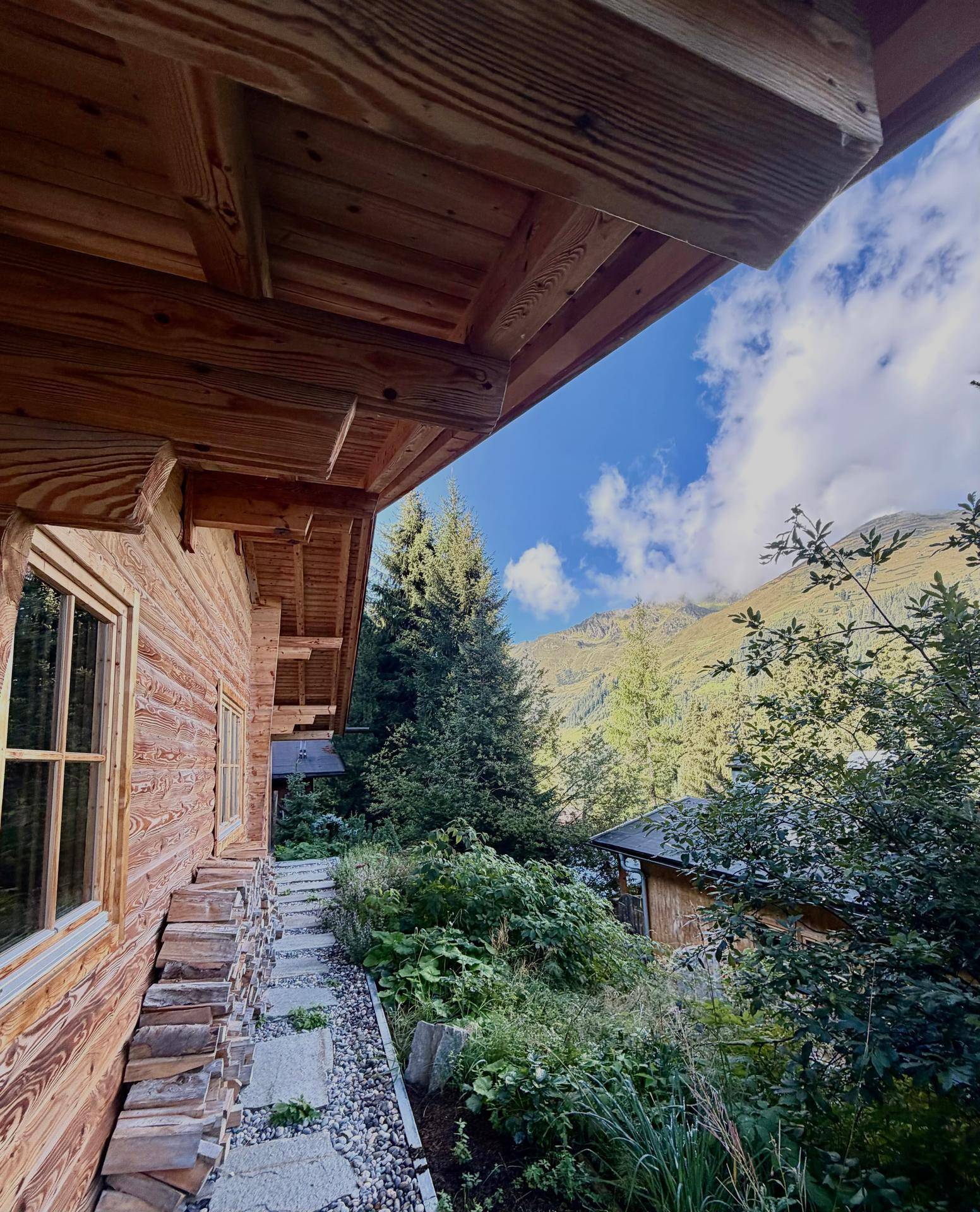 Seitlicher Blick auf das Holzchalet mit einem gepflasterten Weg und üppiger Vegetation.