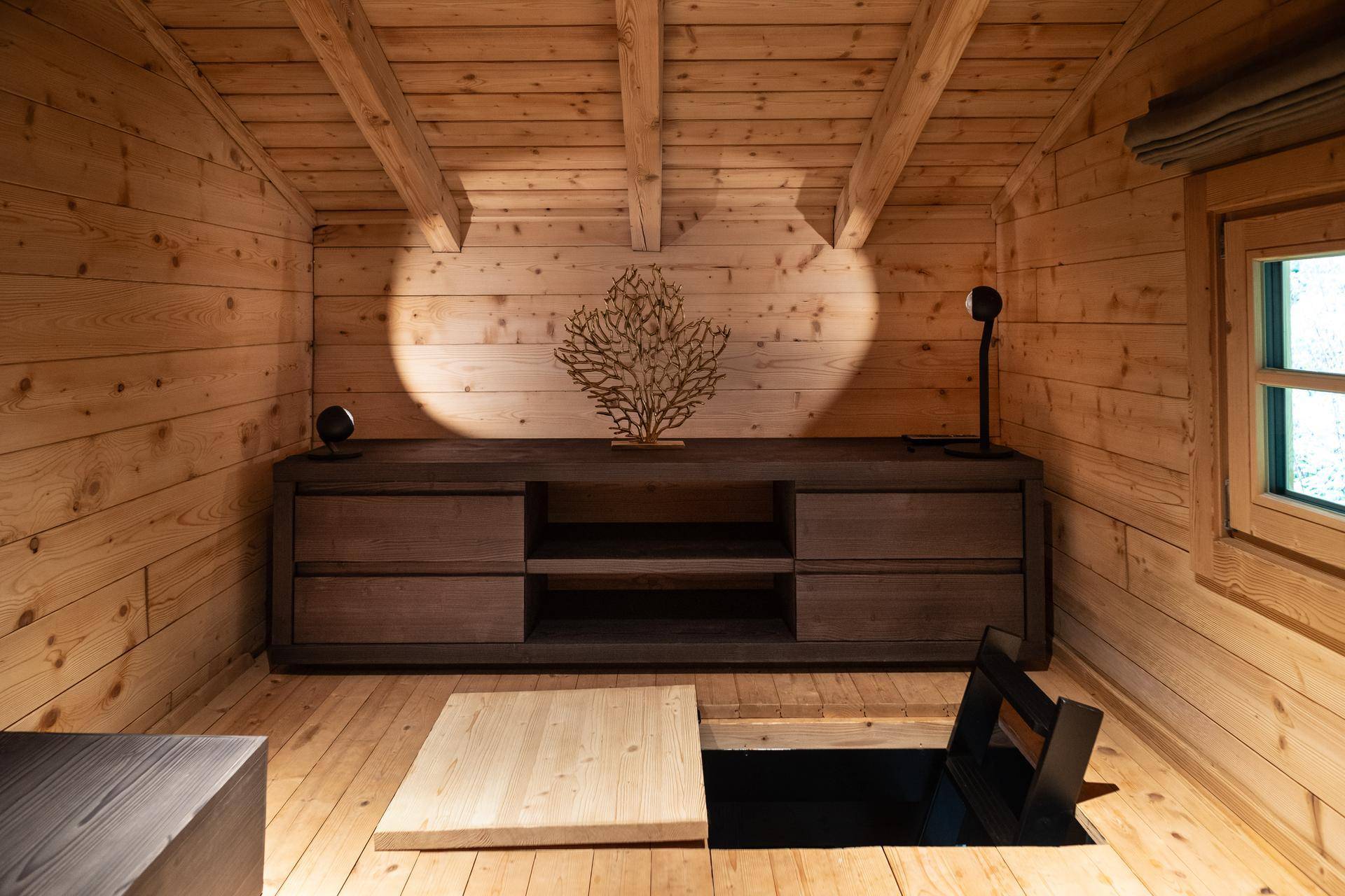 Rustikaler Raum mit Holzwänden, Holzbalkendecke und einem Bodenluken-Zugang.