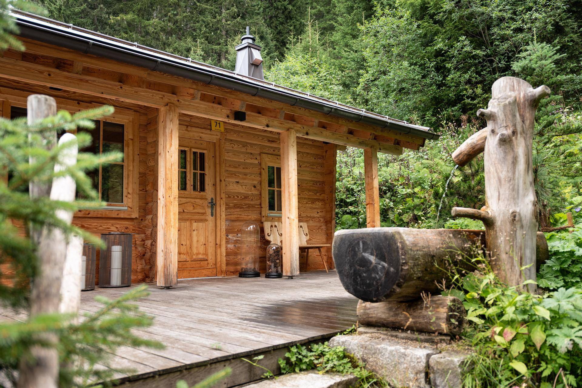 Rustikale Holzterrasse vor einem Chalet mit traditionellem Wasserbrunnen und Waldkulisse.