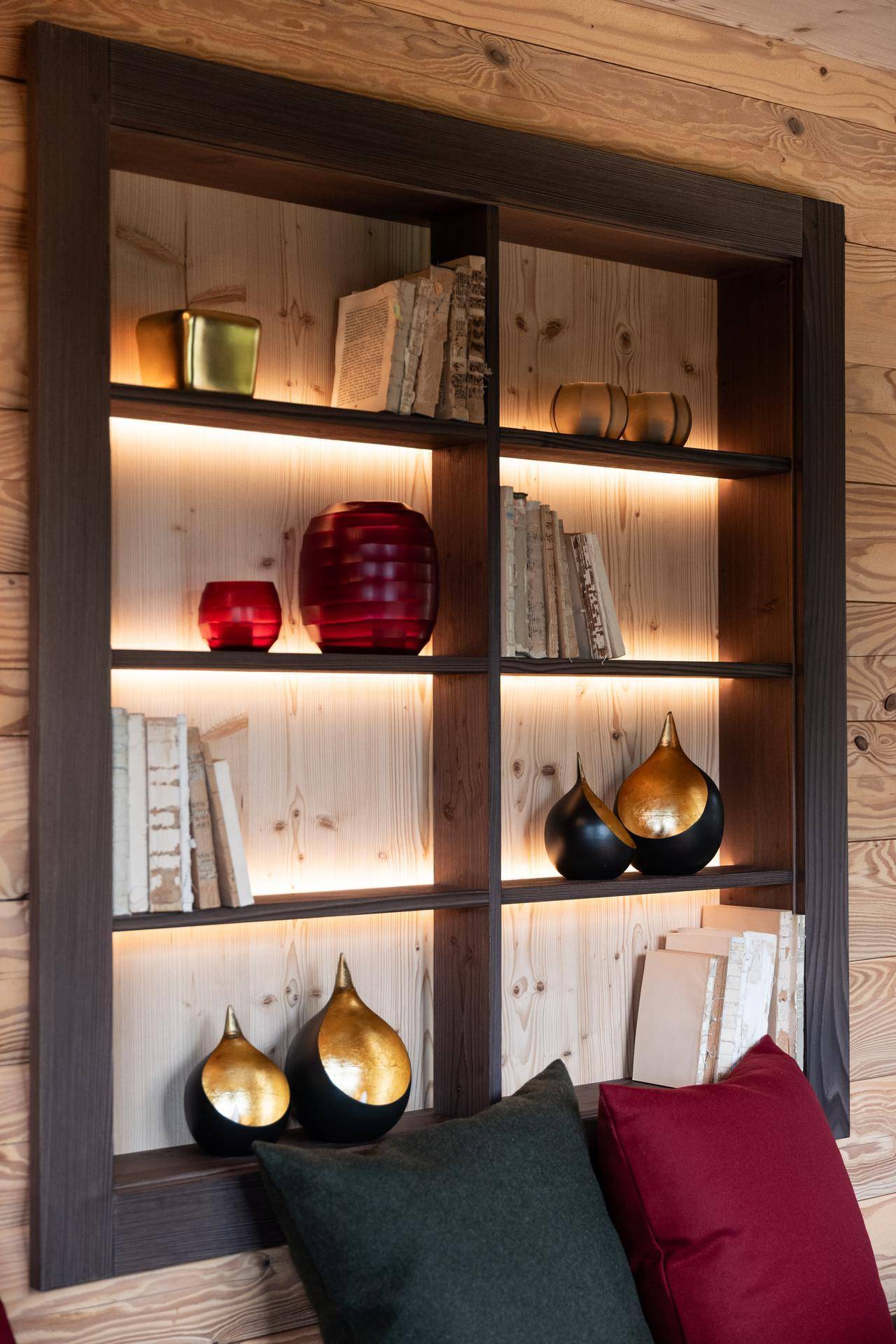 Beleuchtetes Holzregal mit Büchern und dekorativen Elementen in einem gemütlichen Raum.