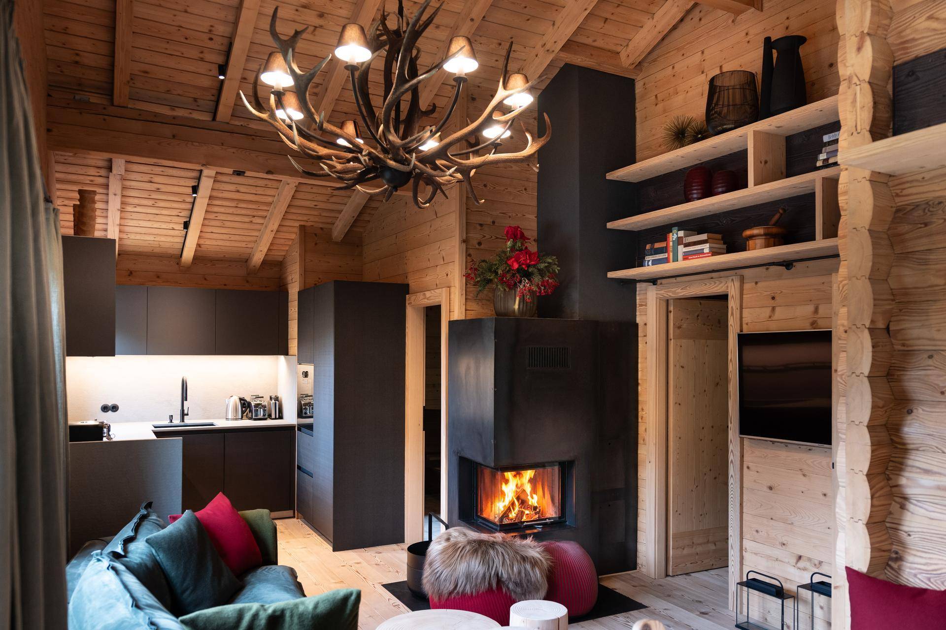 Offener Wohnbereich im Chalet-Stil mit Kamin, Geweihleuchter und moderner Küche.