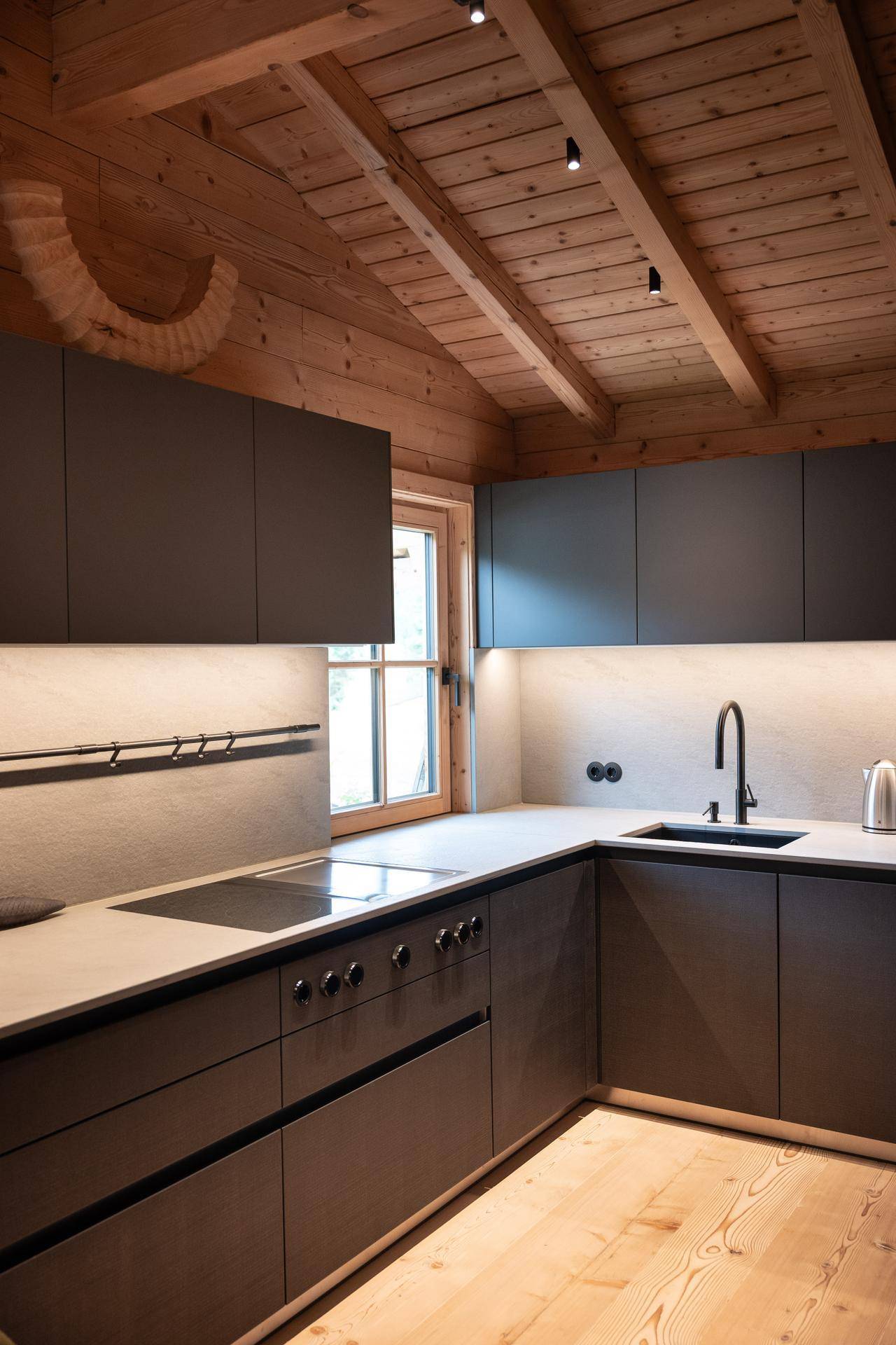 Moderne Küche mit dunklen Schränken, Induktionskochfeld und Holzbalkendecke.