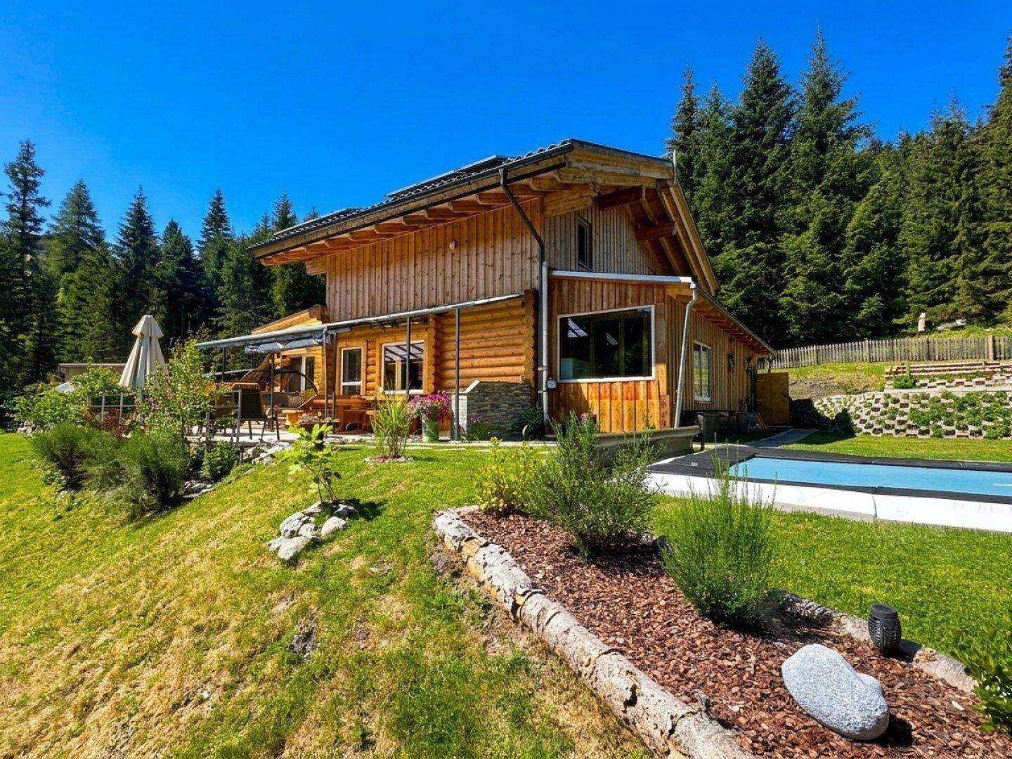 Idyllisches Blockhaus in alpiner Umgebung mit kleinem Pool und weitem Blick auf die bewaldeten Hügel.
