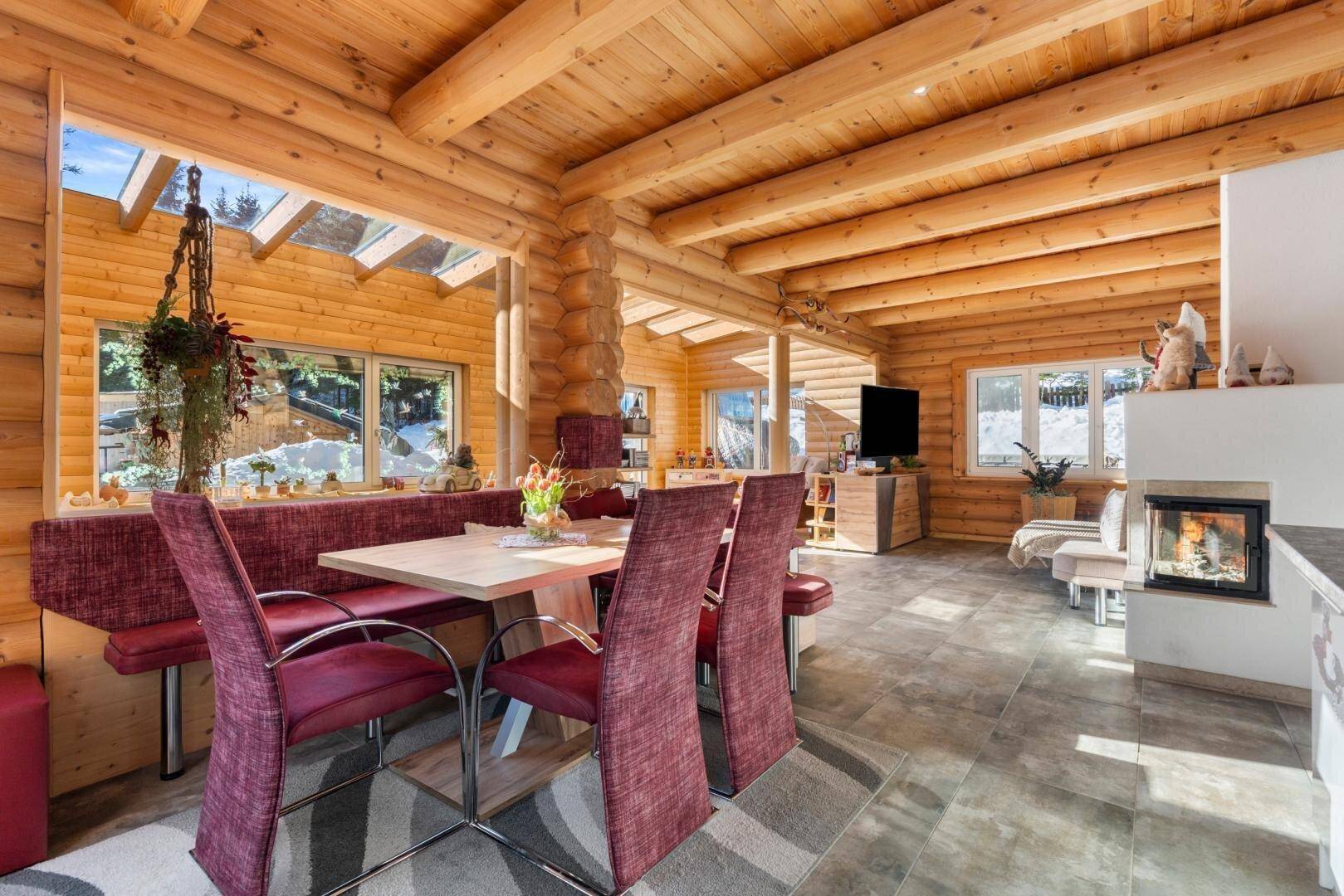 Essbereich mit Holztisch und roten Stühlen, umgeben von Holzvertäfelung und großen Fenstern.