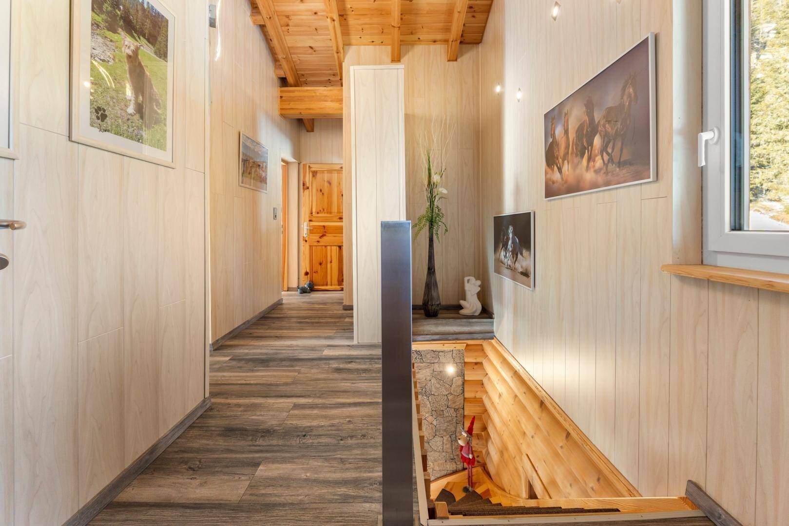 Heller Flur mit Holzvertäfelung, Holzboden und Treppenabgang, geschmückt mit Bildern.