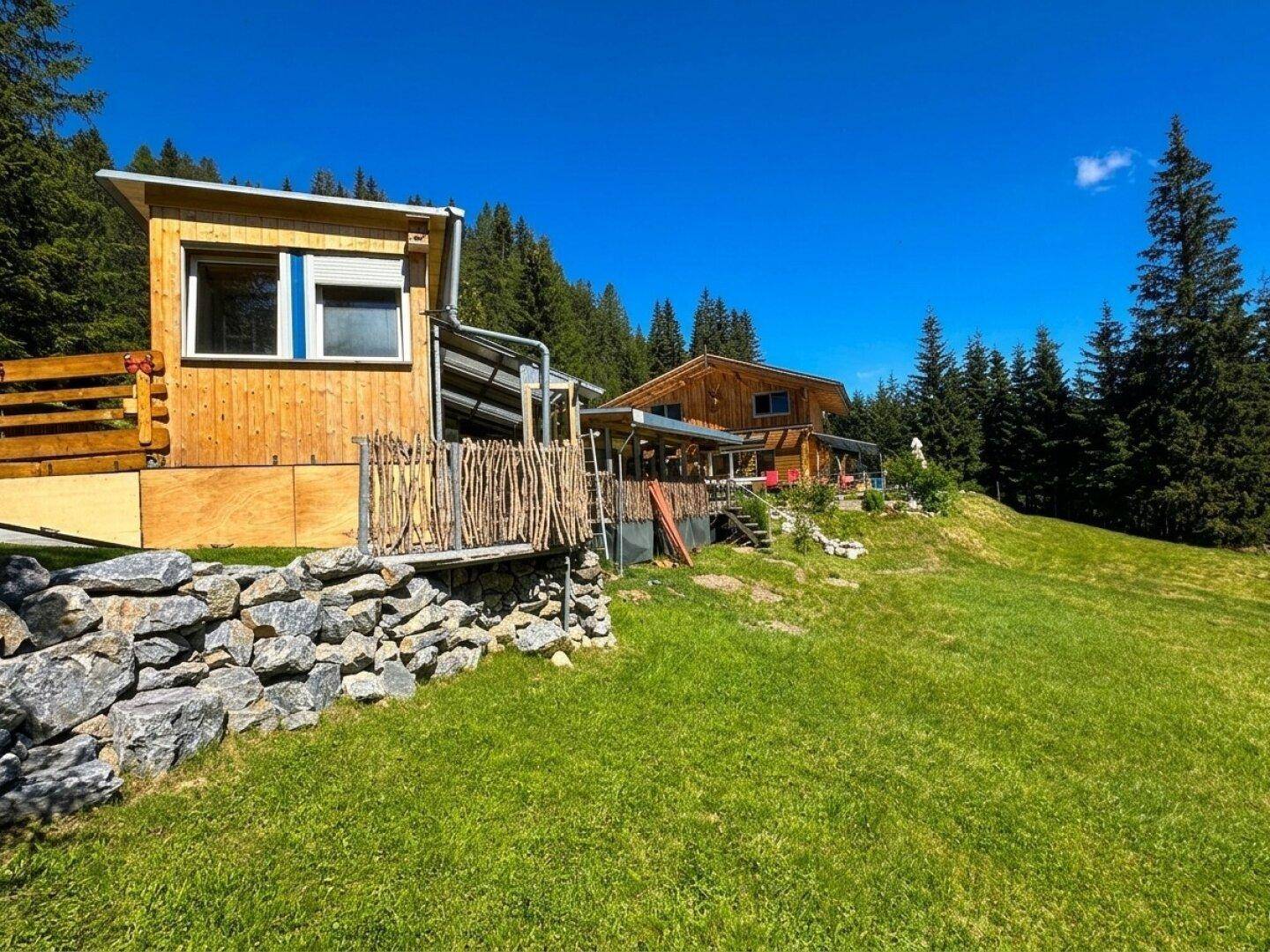 Blockhaus in ländlicher Umgebung mit Nebengebäude und weitem Blick auf die grüne Landschaft.